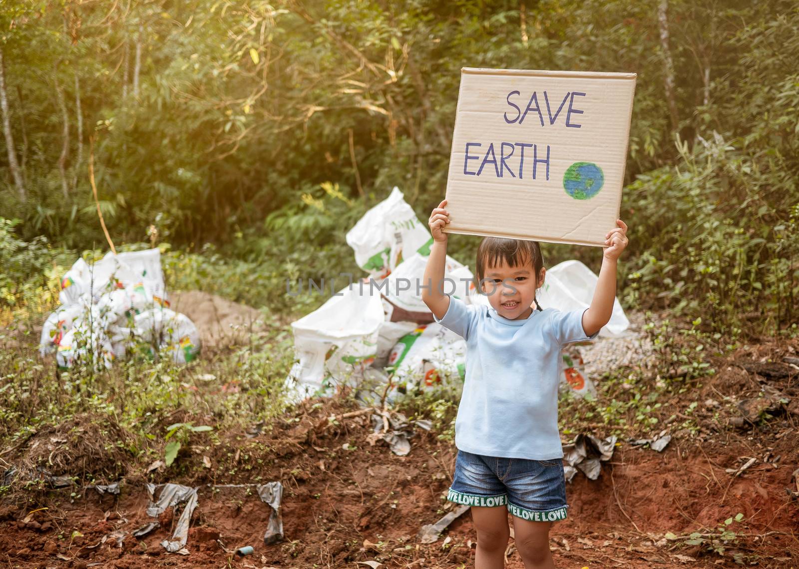 The little child girl holding "Save The Earth" Poster showing a sign protesting against plastic pollution in the forest. The concept of World Environment Day. Zero waste. by TEERASAK