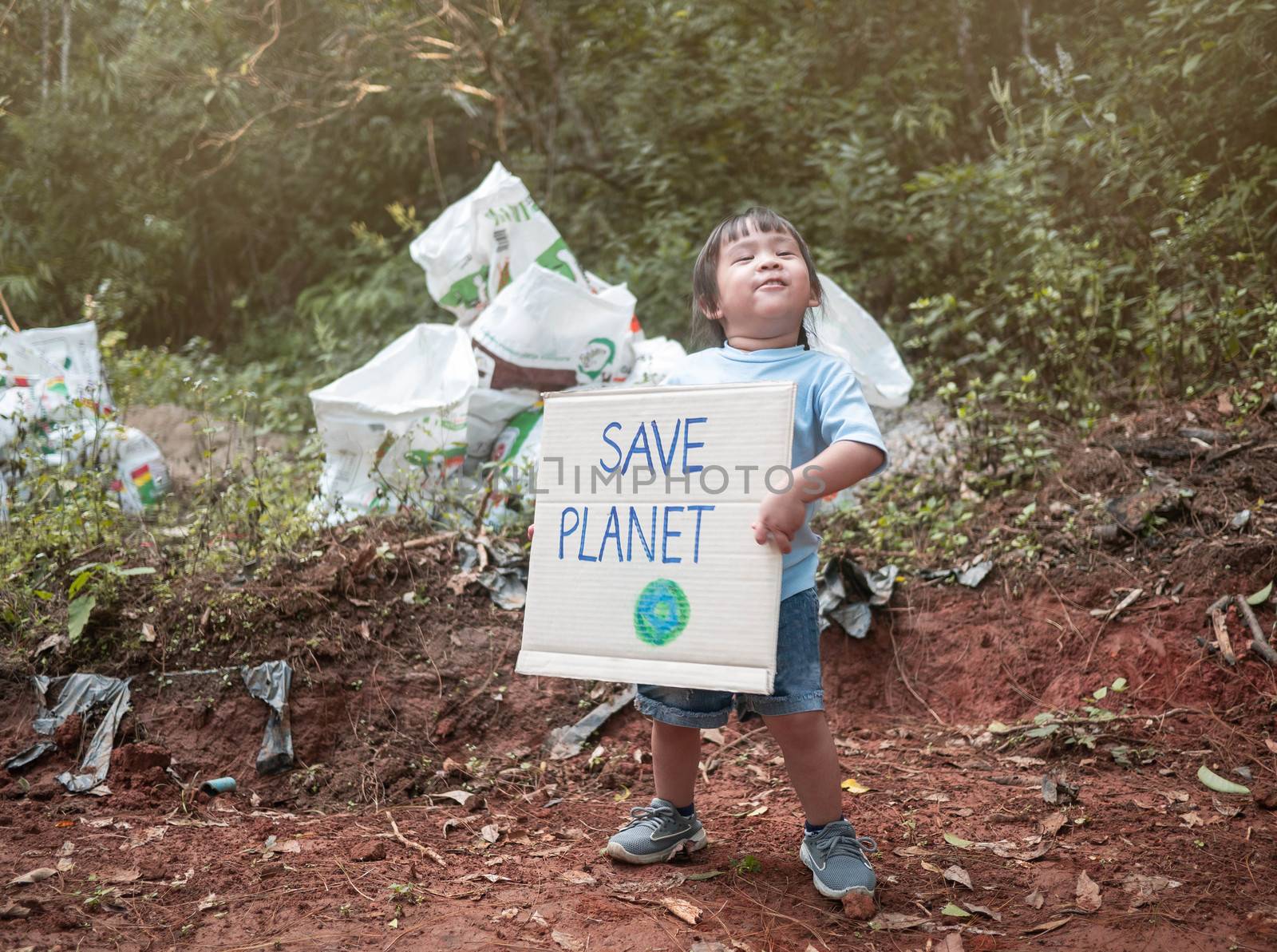 The little child girl holding "Save the planet" Poster showing a sign protesting against plastic pollution in the forest. The concept of World Environment Day. Zero waste. by TEERASAK