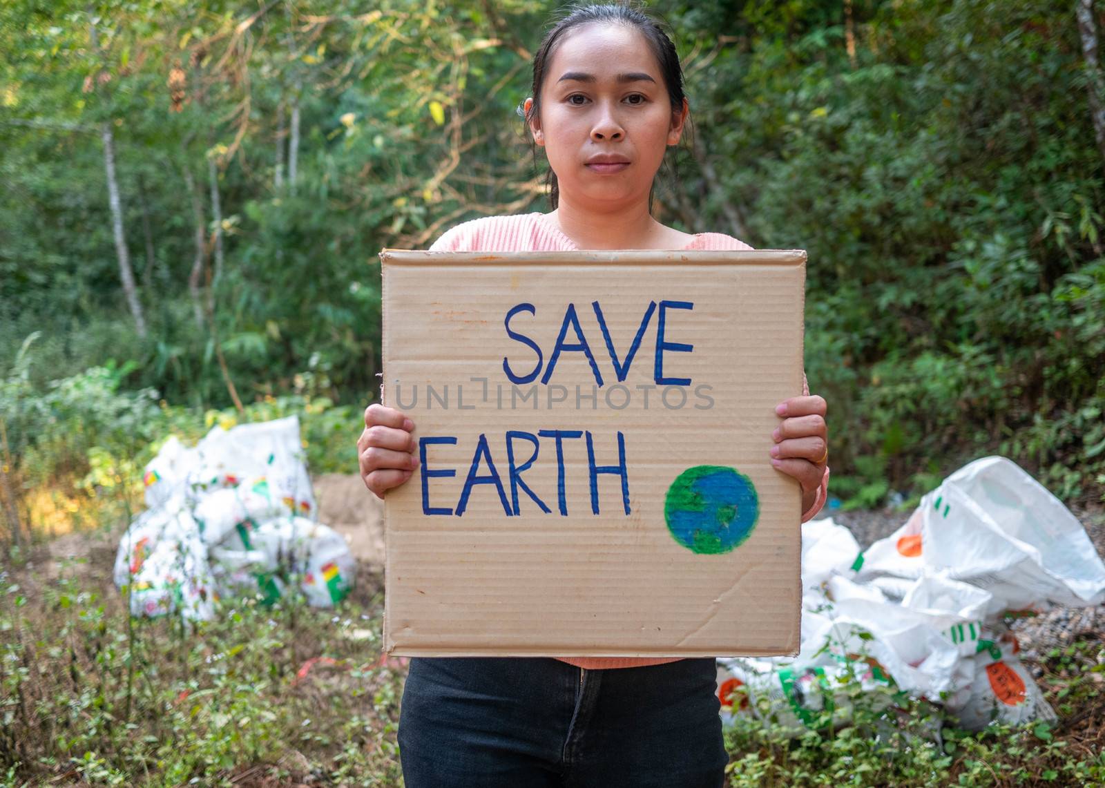 The young woman holding "Save The Earth" Poster showing a sign protesting against plastic pollution in the forest. The concept of World Environment Day. Zero waste. by TEERASAK