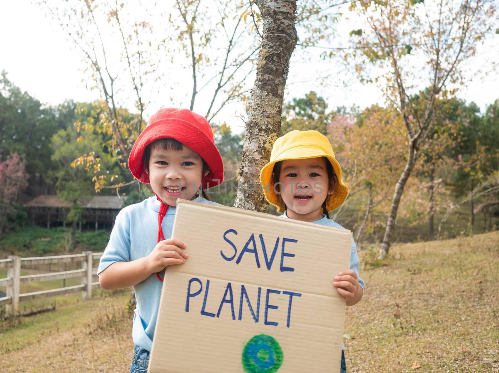 Two little child girl siblings holding "Save the planet" Poster showing a sign protesting against plastic pollution in the forest. The concept of World Environment Day. Zero waste. by TEERASAK