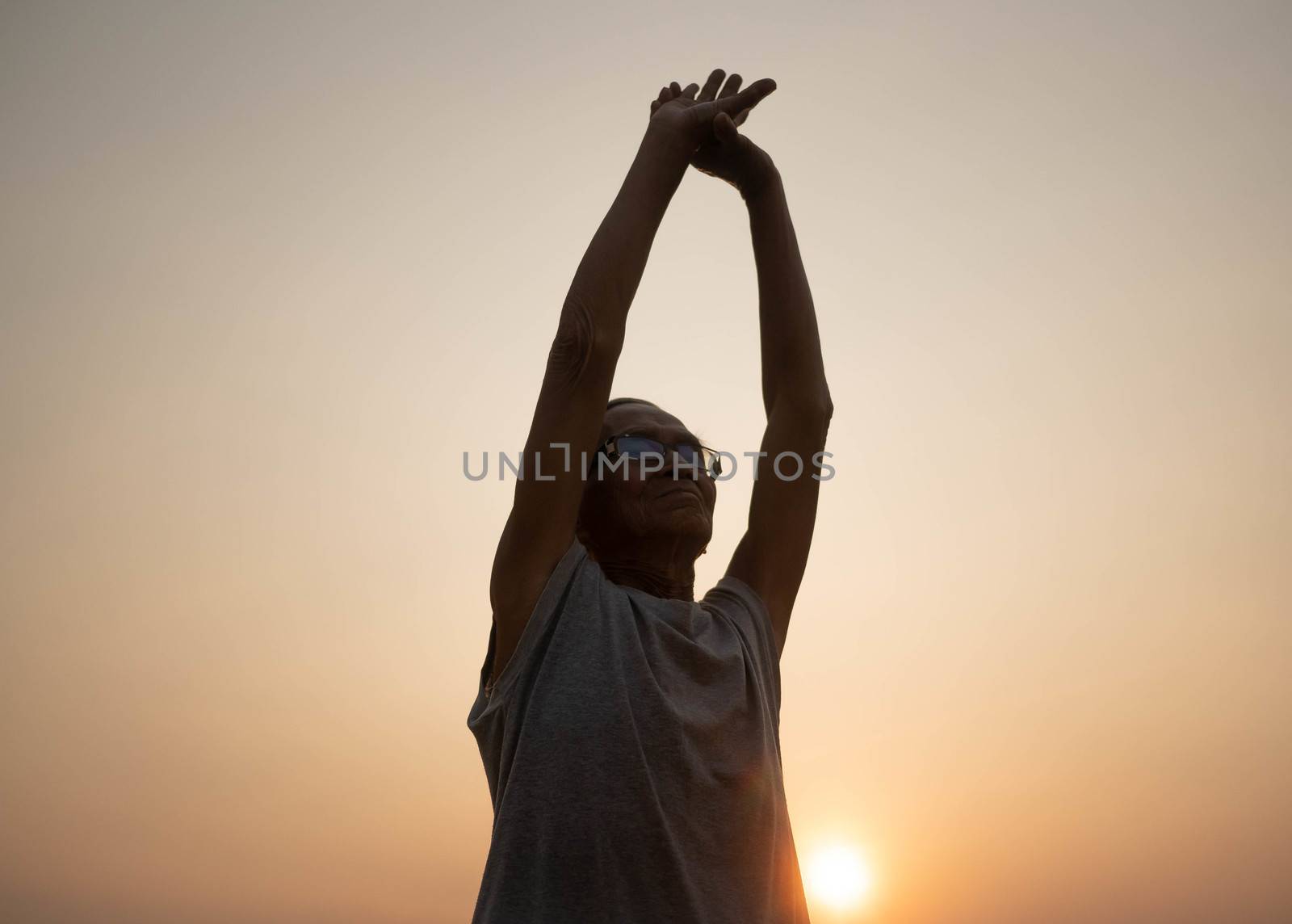 Asian senior man is stretching before running workout in the park on sunset background. Healthcare concept.