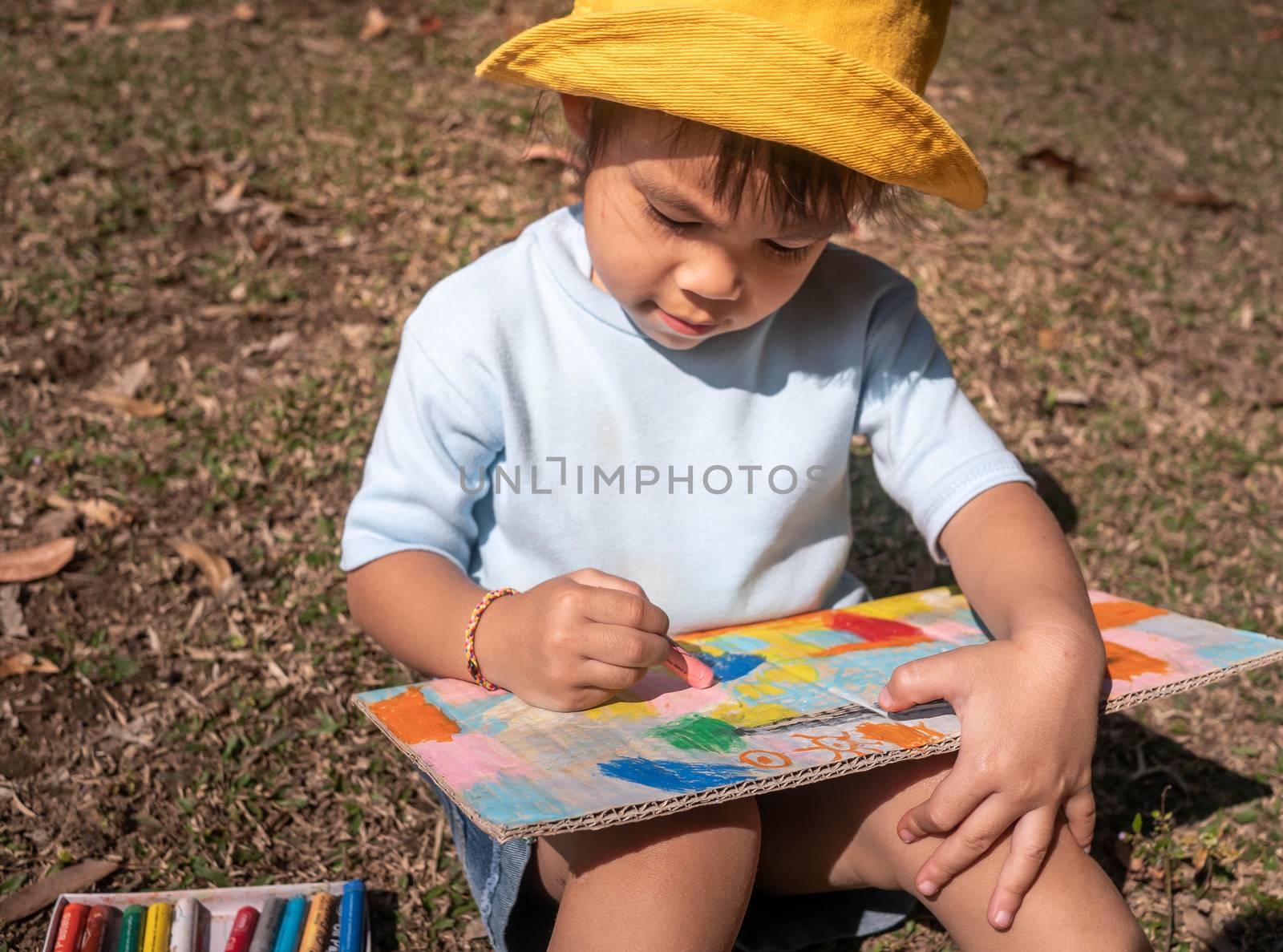 The artist little child girl sitting and painting in the recycling cardboard in a summer park.