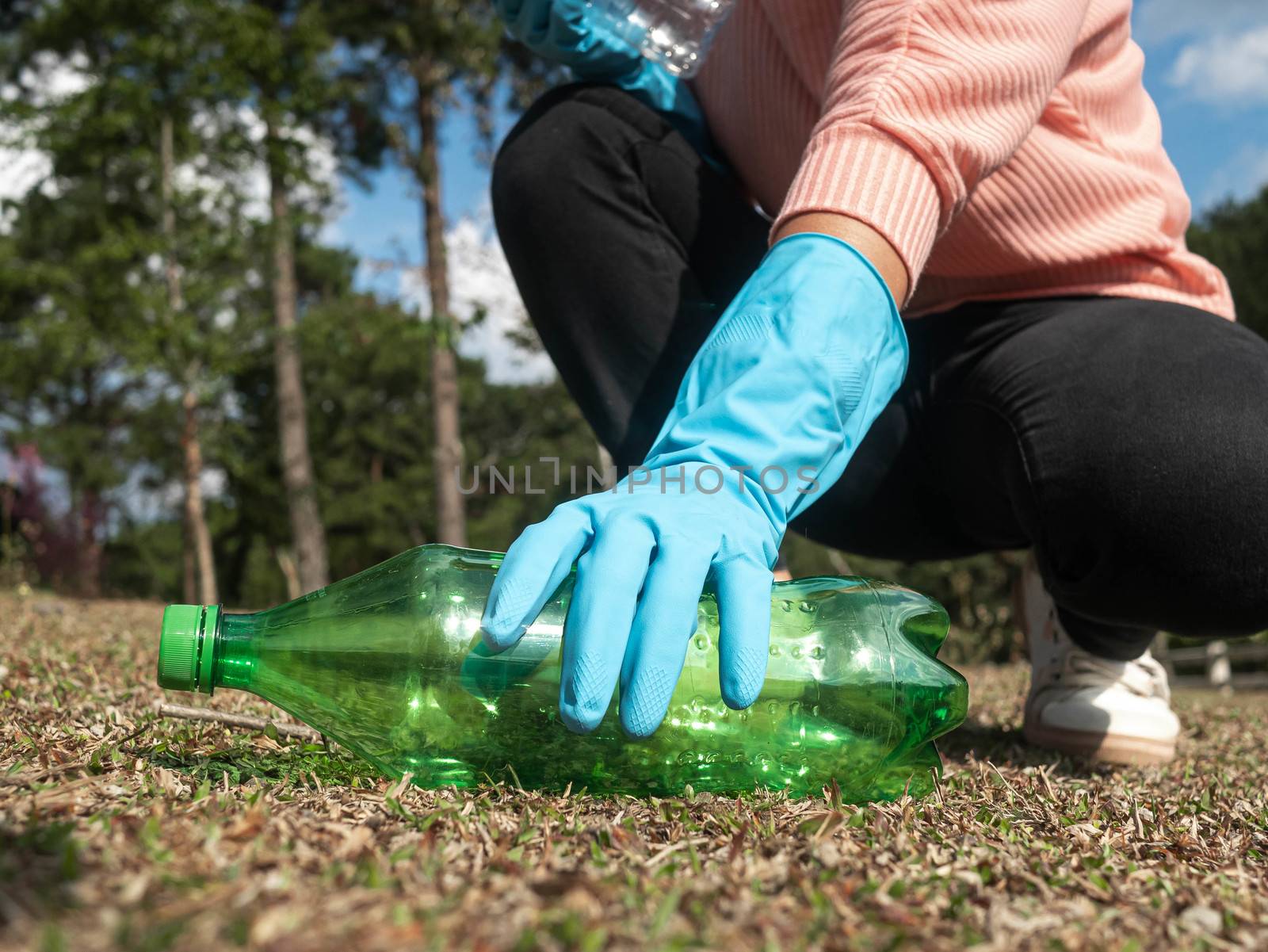 Close up hand of volunteer in gloves picks up a plastic bottle from the grass in the park. Concepts of save environment and stop plastic pollution. by TEERASAK