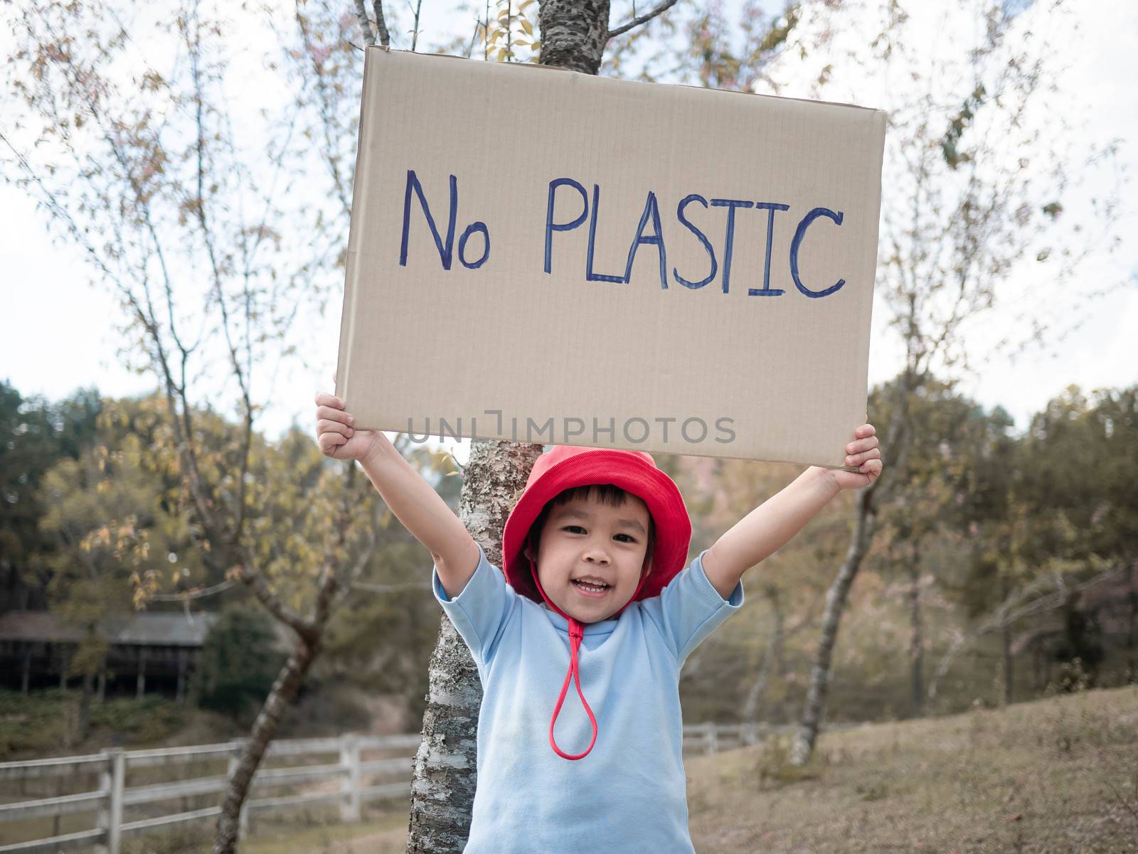 The little child girl holding "No Plastic" Poster showing a sign protesting against plastic pollution in the forest. The concept of World Environment Day. Zero waste. by TEERASAK
