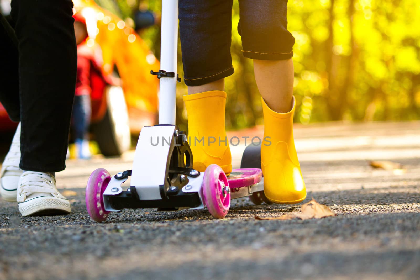 Cute little child girl having fun to riding a scooter on road with her mother in a summer park. Concept of happy family and childhood. Close up shot of legs of people in garden.