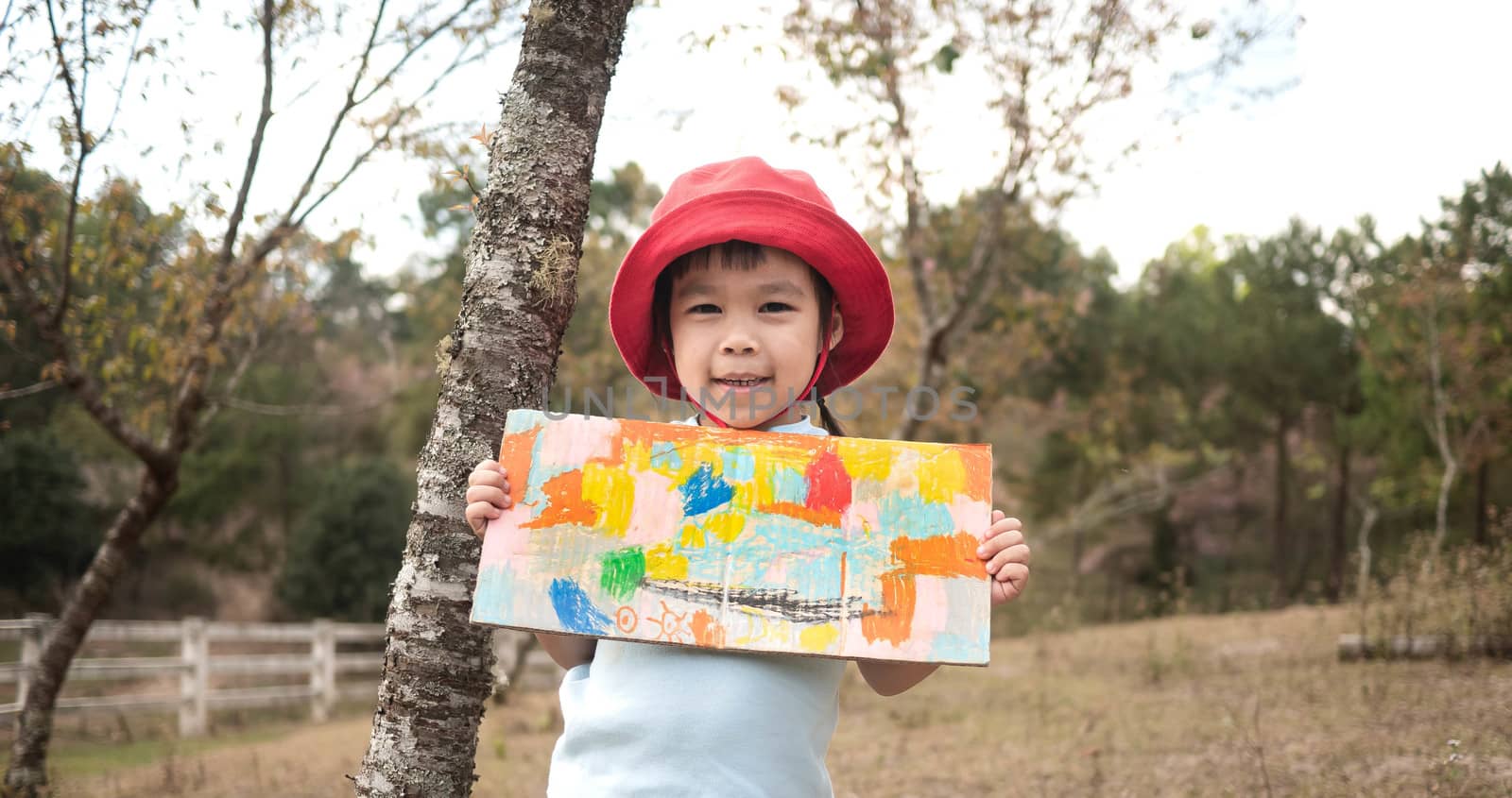 Happy little girl showing her coloring work in cardboard in the garden.