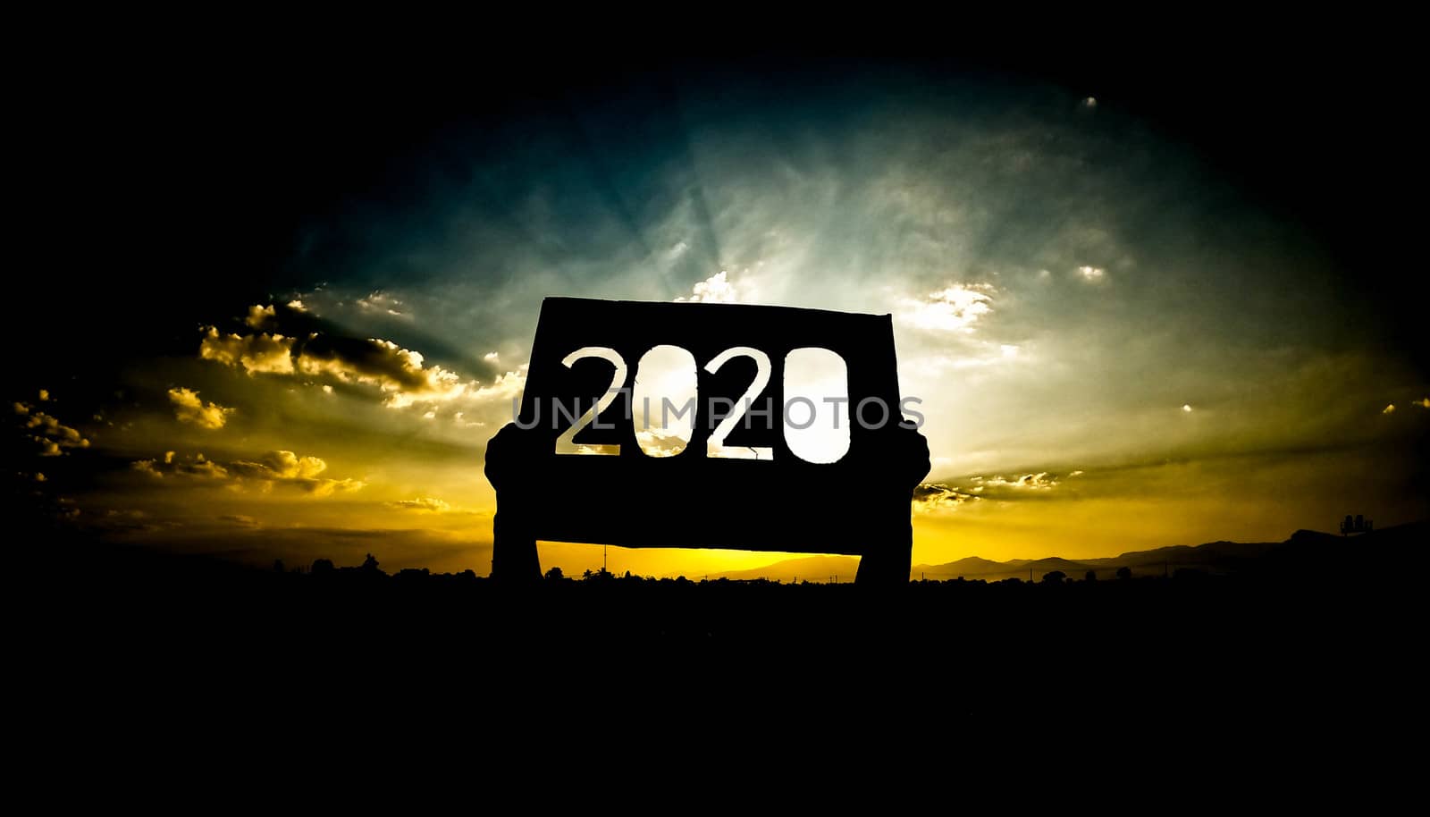 Silhouette of hands holding recycle cardboard with 2020 text over sunset sky background and the sun shining through the text. Concepts of New Year and celebration.