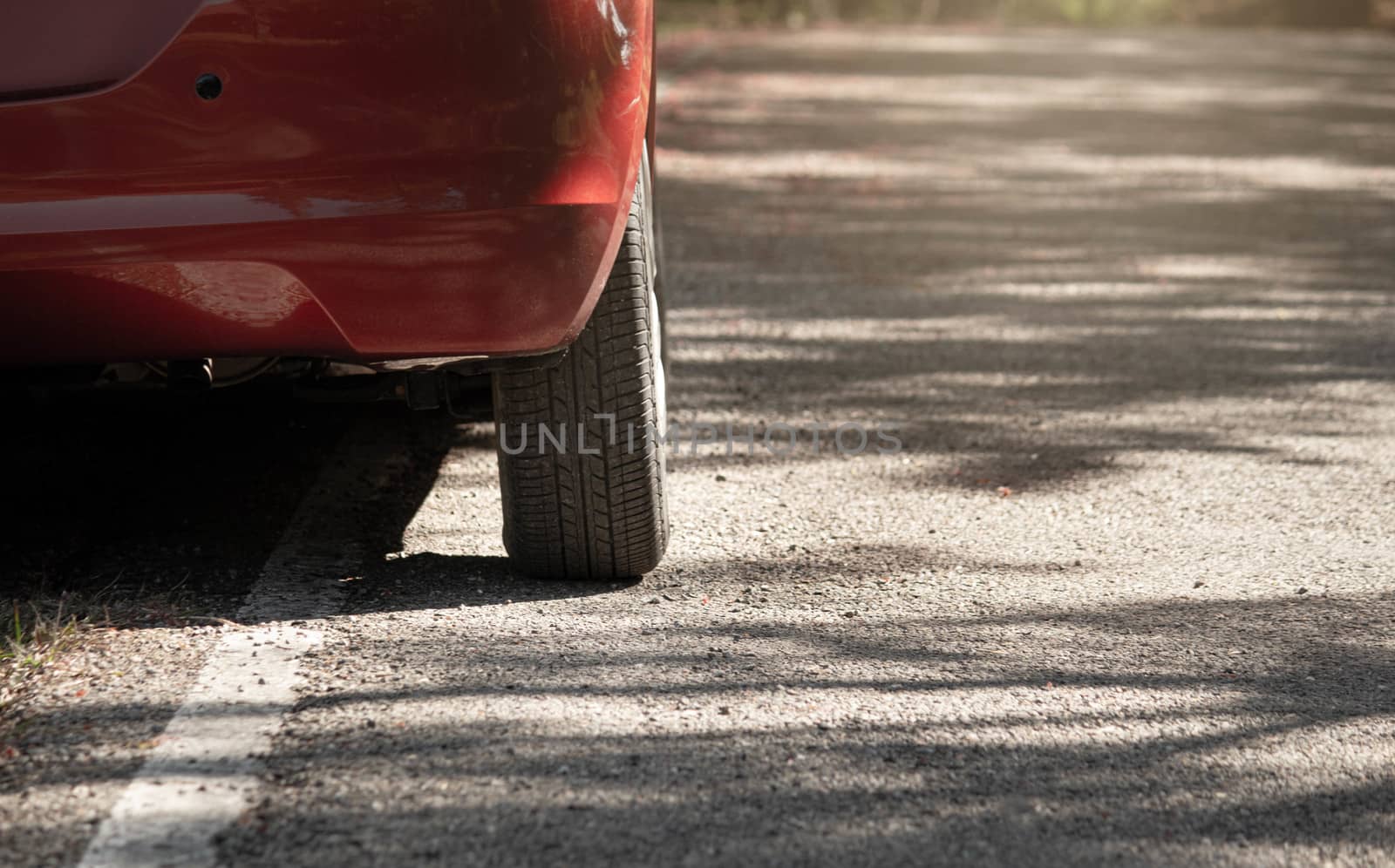Rear wheel tire of red car parked on the side of the asphalt road. by TEERASAK