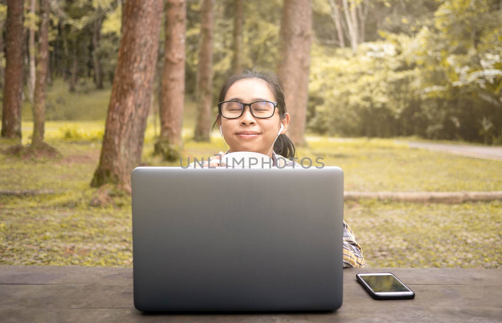 Happy casual beautiful woman working on laptop and drinking coffee while sitting in national park.
