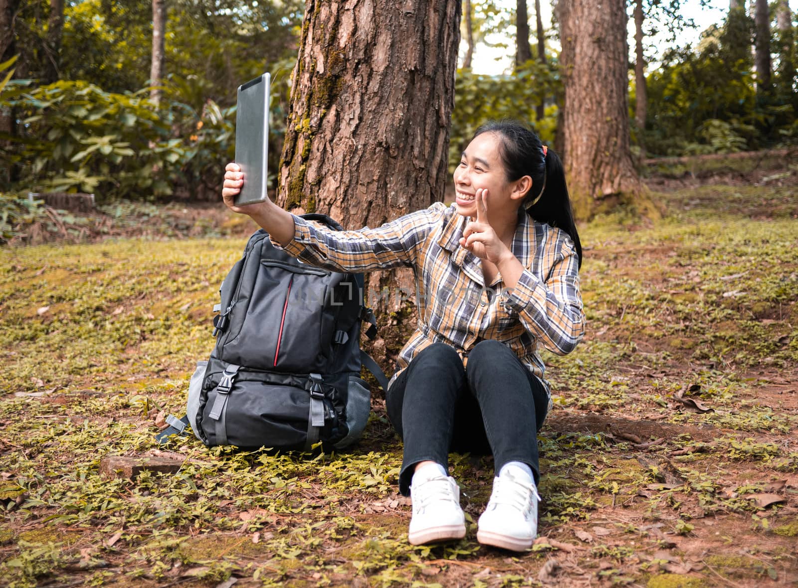 Young woman traveler selfie by using tablet while sit and rest in forest on summer vacations day. Lifestyle hiking concept.