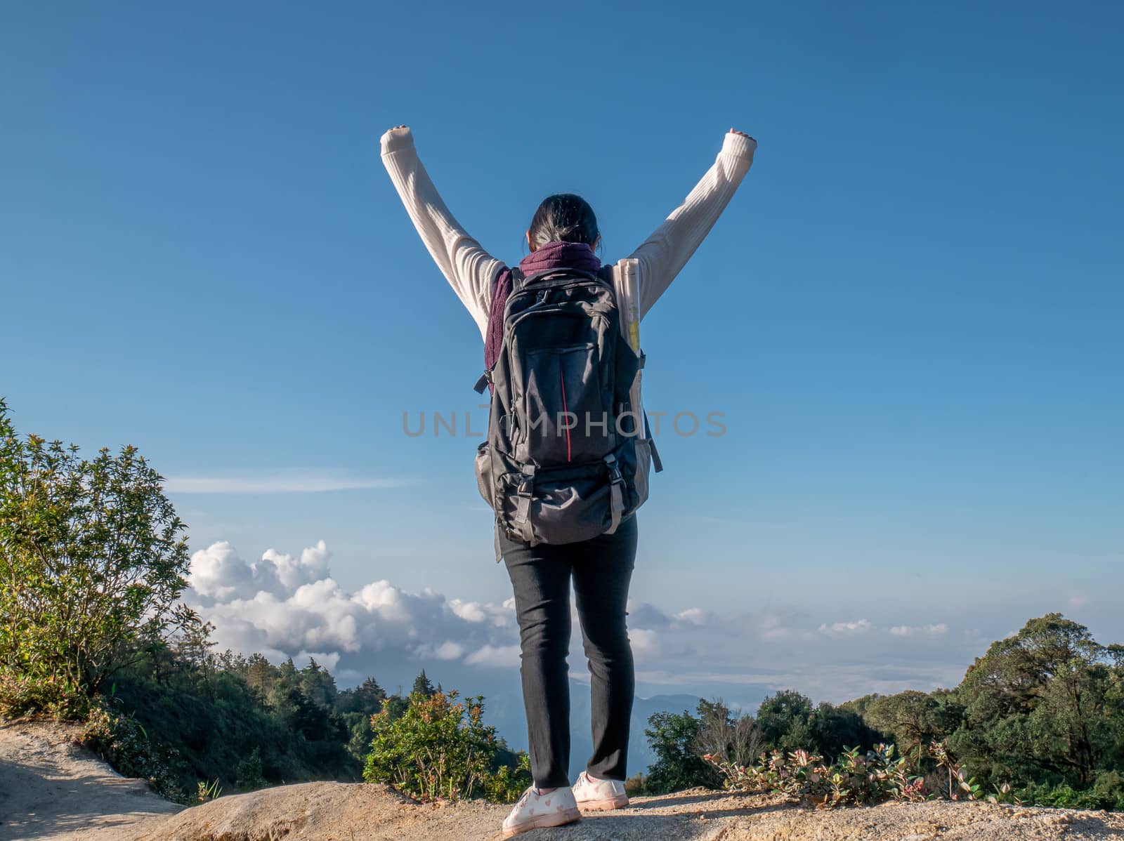 Young woman traveler raise arms to show success at peak of mountains on summer vacations day. Lifestyle hiking concept. by TEERASAK