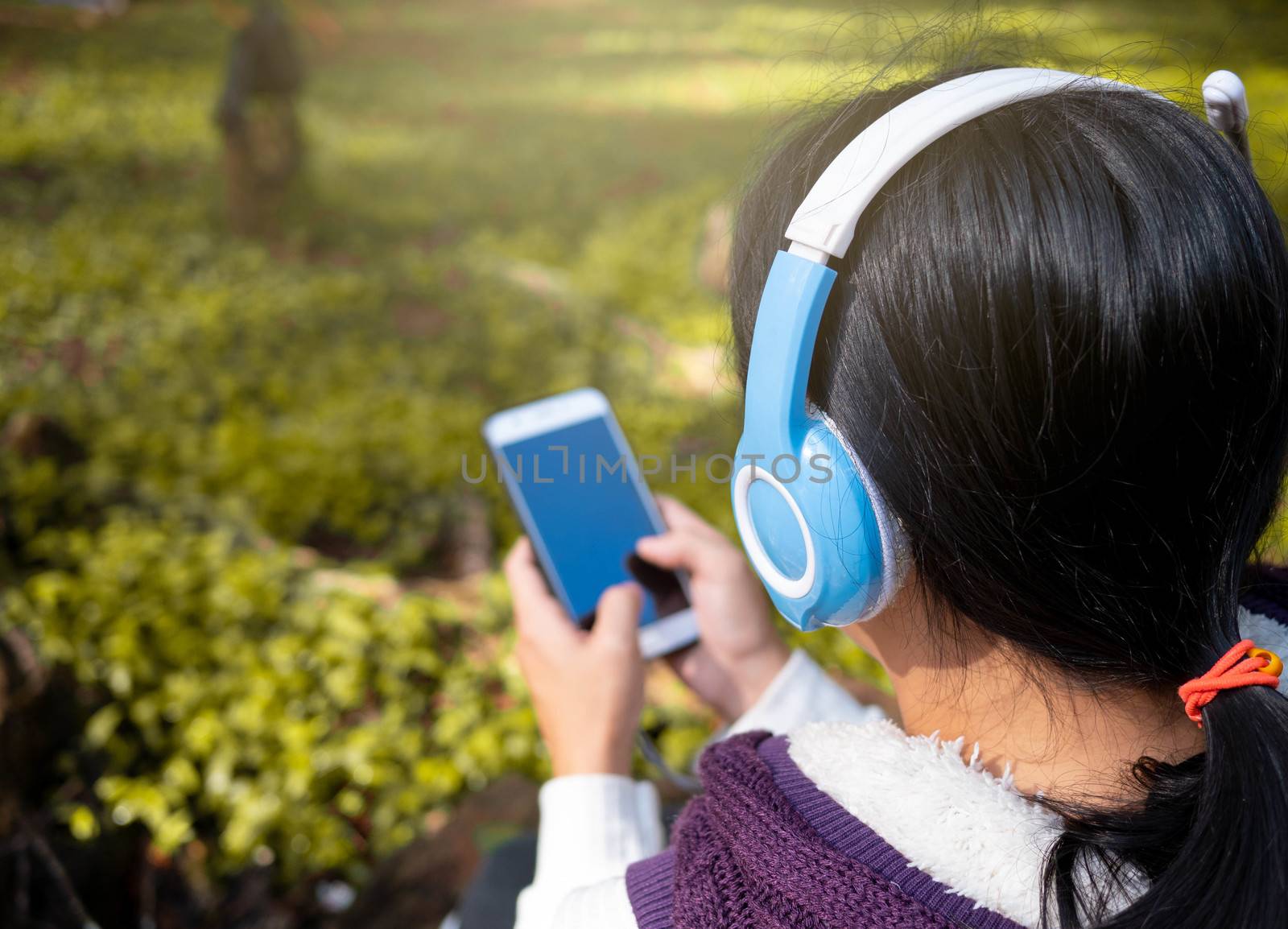 Asian young girl listening to music by headphone in the garden. Asian young girl listening to music by headphone in the garden. Technology and relaxation concept. by TEERASAK