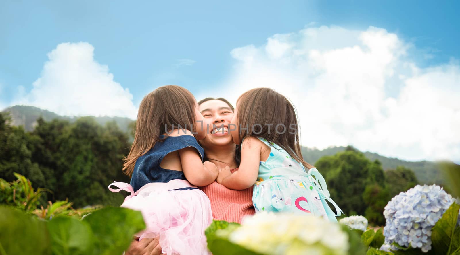 Happy family in hydrangea garden over trees with mountains background under blue sky in summer day.