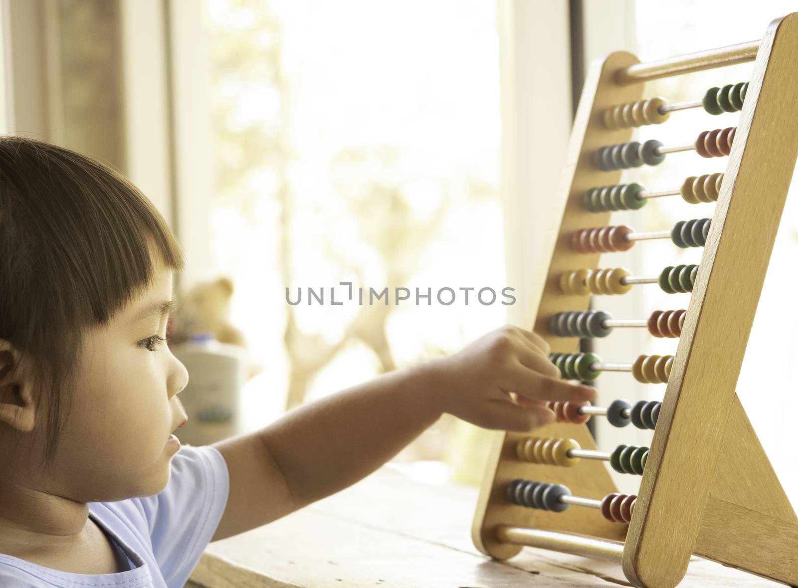 Lovely little girl learning with educational colorful wooden abacus and counting indoors. Home school of preschool children concept.