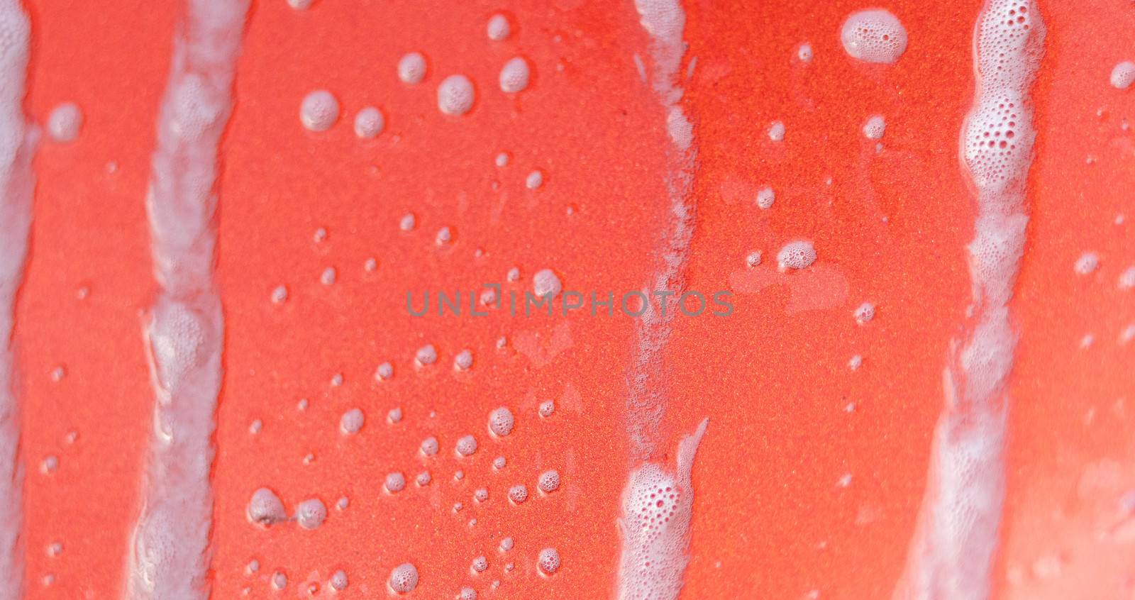 Bubble soap on the red car. Car washing concept.