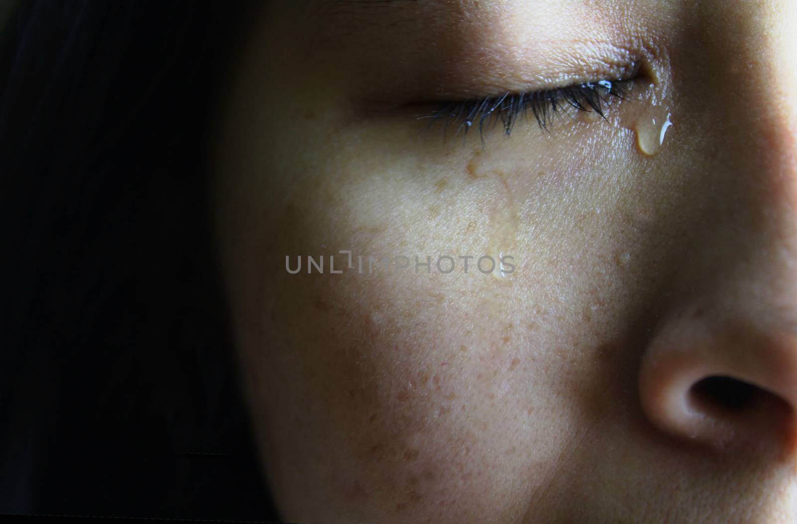 Close-up half face of Asian woman crying with tears, isolated on dark background. Concepts of emotion and expression of human. by TEERASAK