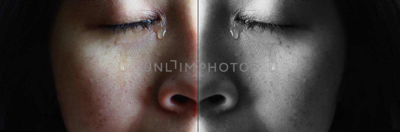 Close-up face of Asian woman crying with tears, isolated on dark background. Concepts of emotion and expression of human.