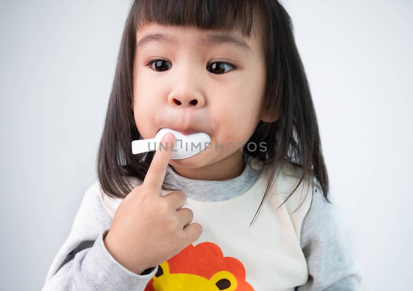 Cute sick little girl taking medicine isolated on gray backgroun by TEERASAK