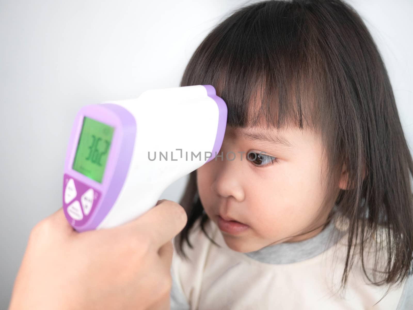 Close up of mother hand checking temperature of her sick daughter by electronic medical infrared thermometer, Isolated on gray background. Concept of healthcare and medical in child.