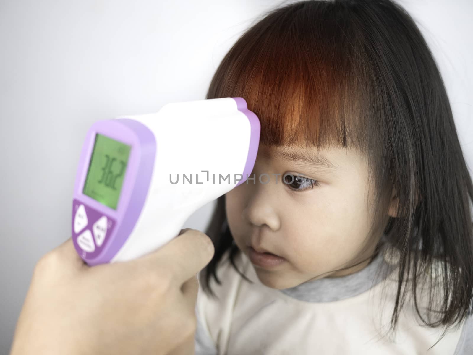 Close up of mother hand checking temperature of her sick daughter by electronic medical infrared thermometer, Isolated on gray background. Concept of healthcare and medical in child.