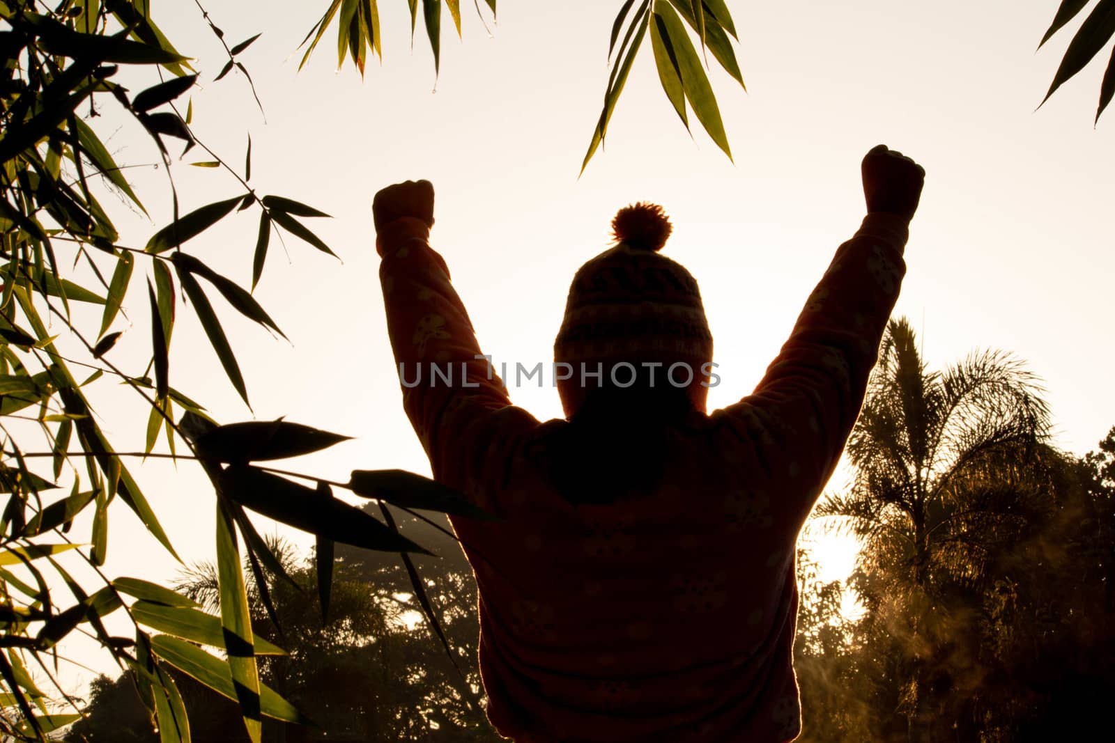 The silhouette of Happy beautiful young woman with raised arms enjoying the nature in winter time at sunrise background.