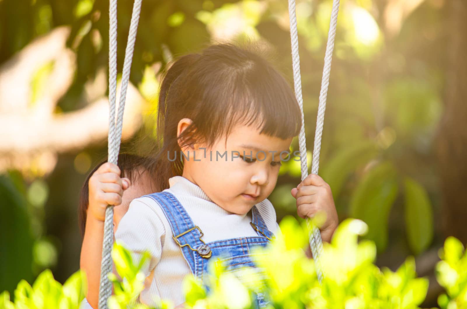 Cute happy child girl enjoy playing bamboo swing in the backyard.