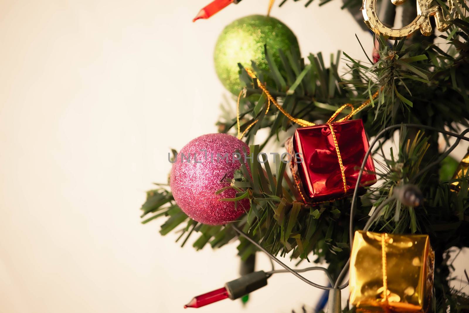 Close up of pink bauble hanging from a decorated Christmas tree with lights presents for new year isolated on white background.