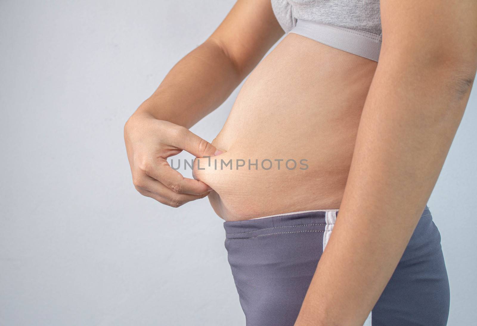 Close-up side view of woman's hand pinching excessive belly fat  by TEERASAK