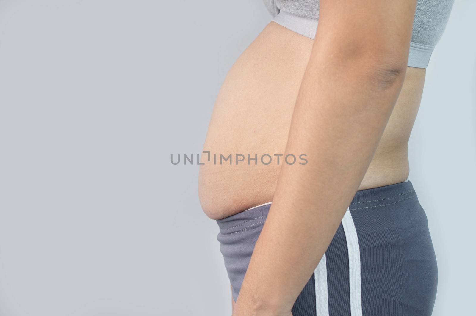 Close-up side view of woman excessive belly fat isolated on gray background. Woman fat belly. Obesity and Overweight Concept.