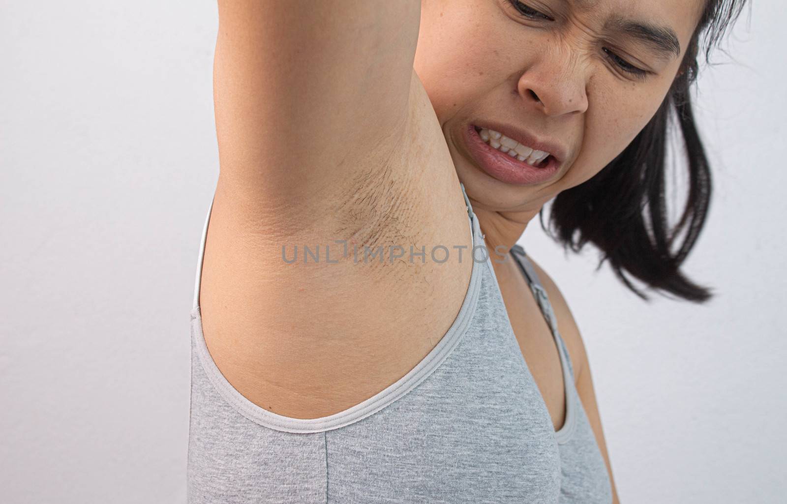 Close up of young woman showing her unshaved armpit and offensive face isolated on grey background. Concept of Health care for skin and beauty.