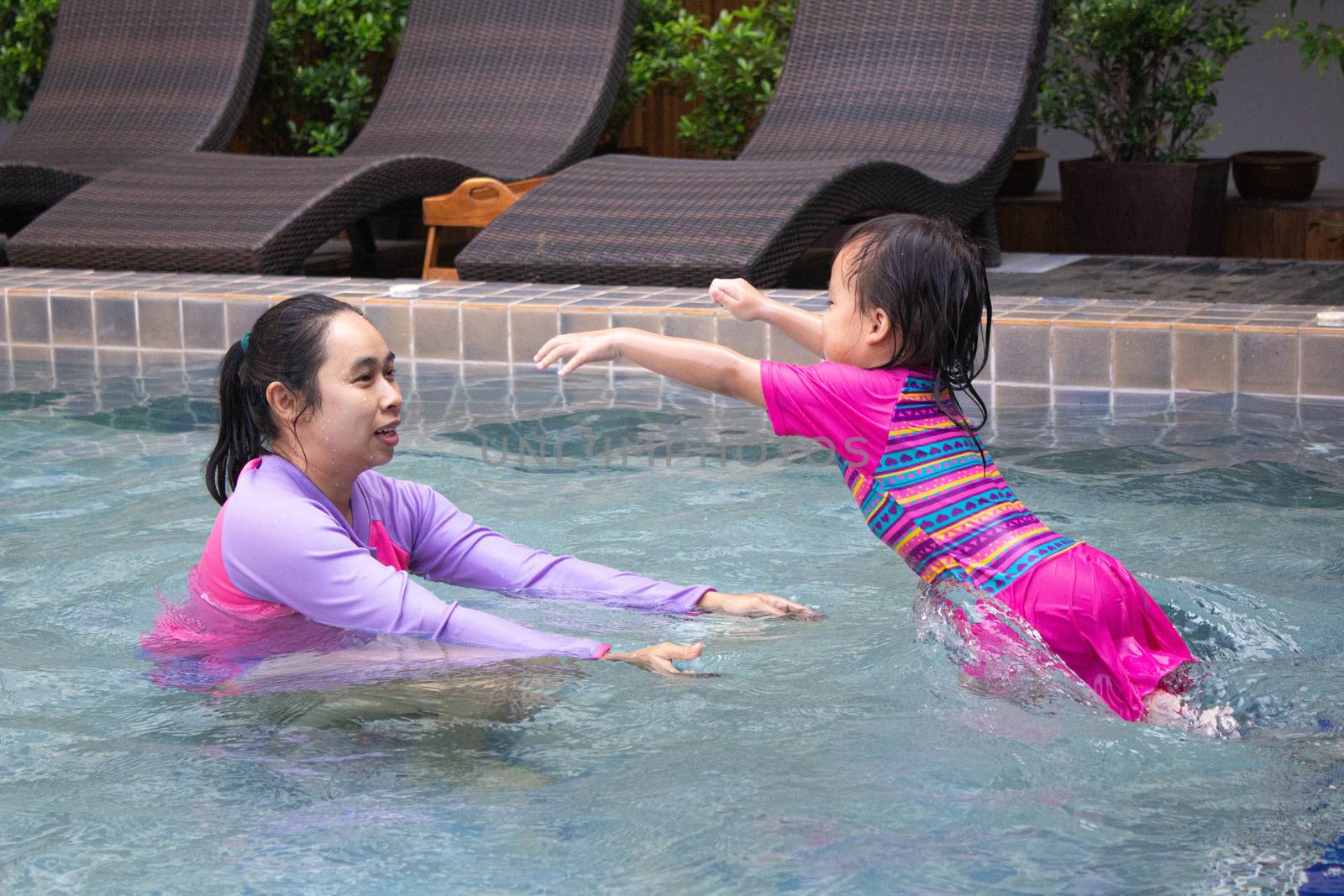 Happy Asian family enjoying summer vacation in swimming pool at resort. by TEERASAK