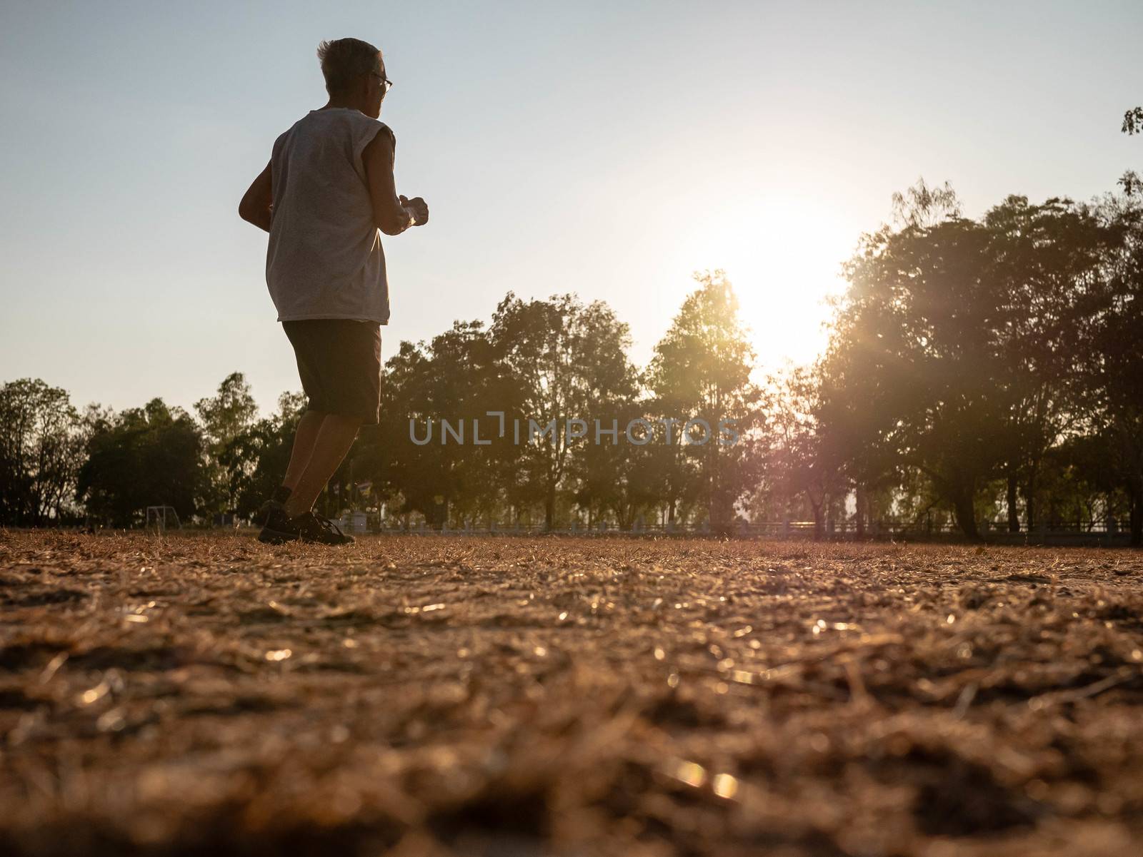Asian senior man jogging in the park over sunset sky background. Healthy lifestyle and Healthcare concept.