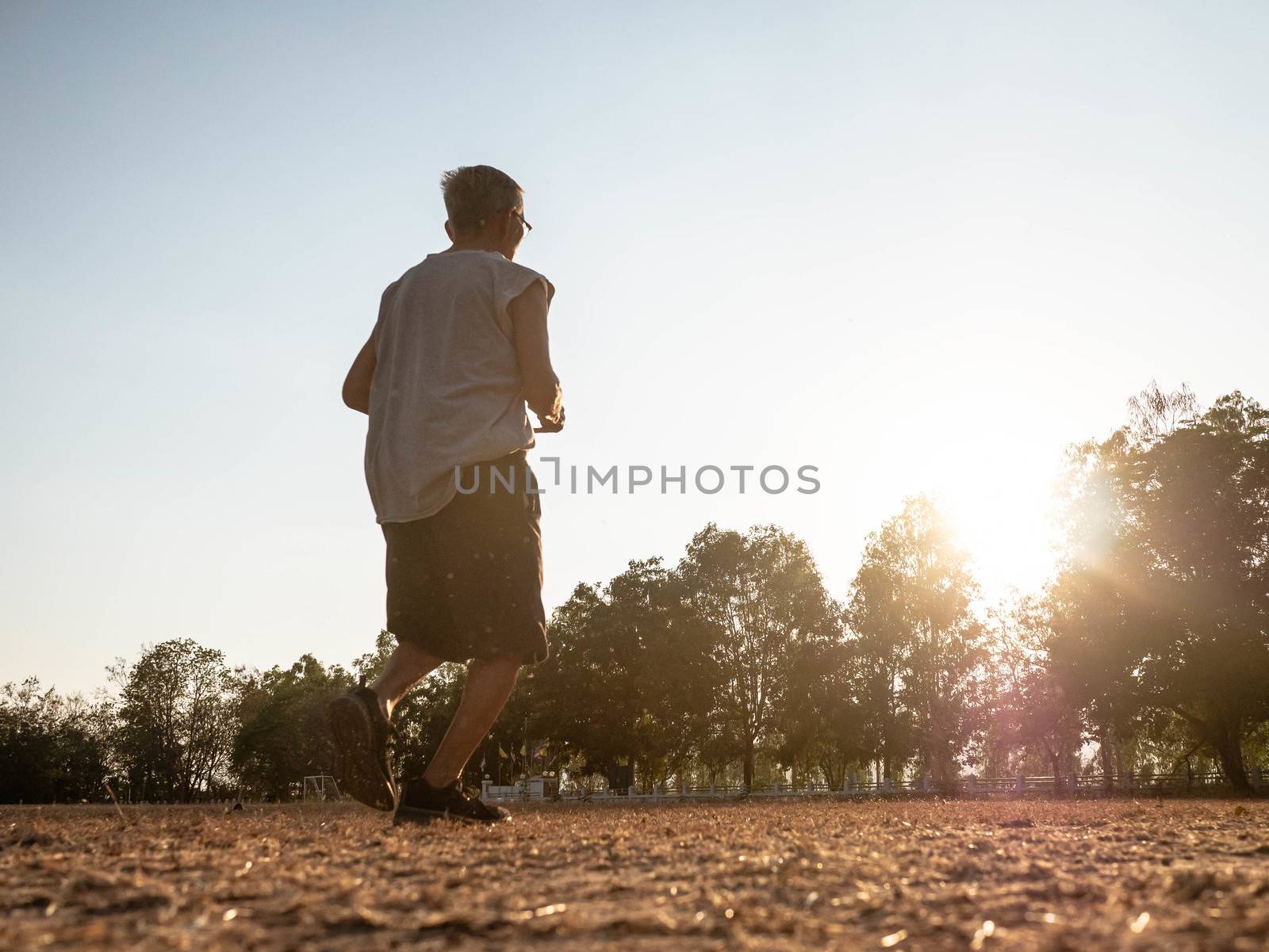 Asian senior man jogging in the park over sunset sky background.Asian senior man jogging in the park over sunset sky background. Healthy lifestyle and Healthcare concept. by TEERASAK