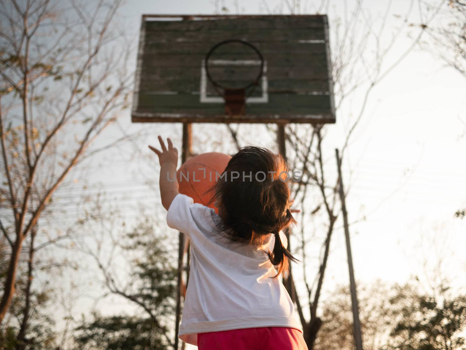 Cute little Asian child playing basketball on playground on summCute little Asian child playing basketball on playground on summer day. Healthy outdoor sport for young child. by TEERASAK