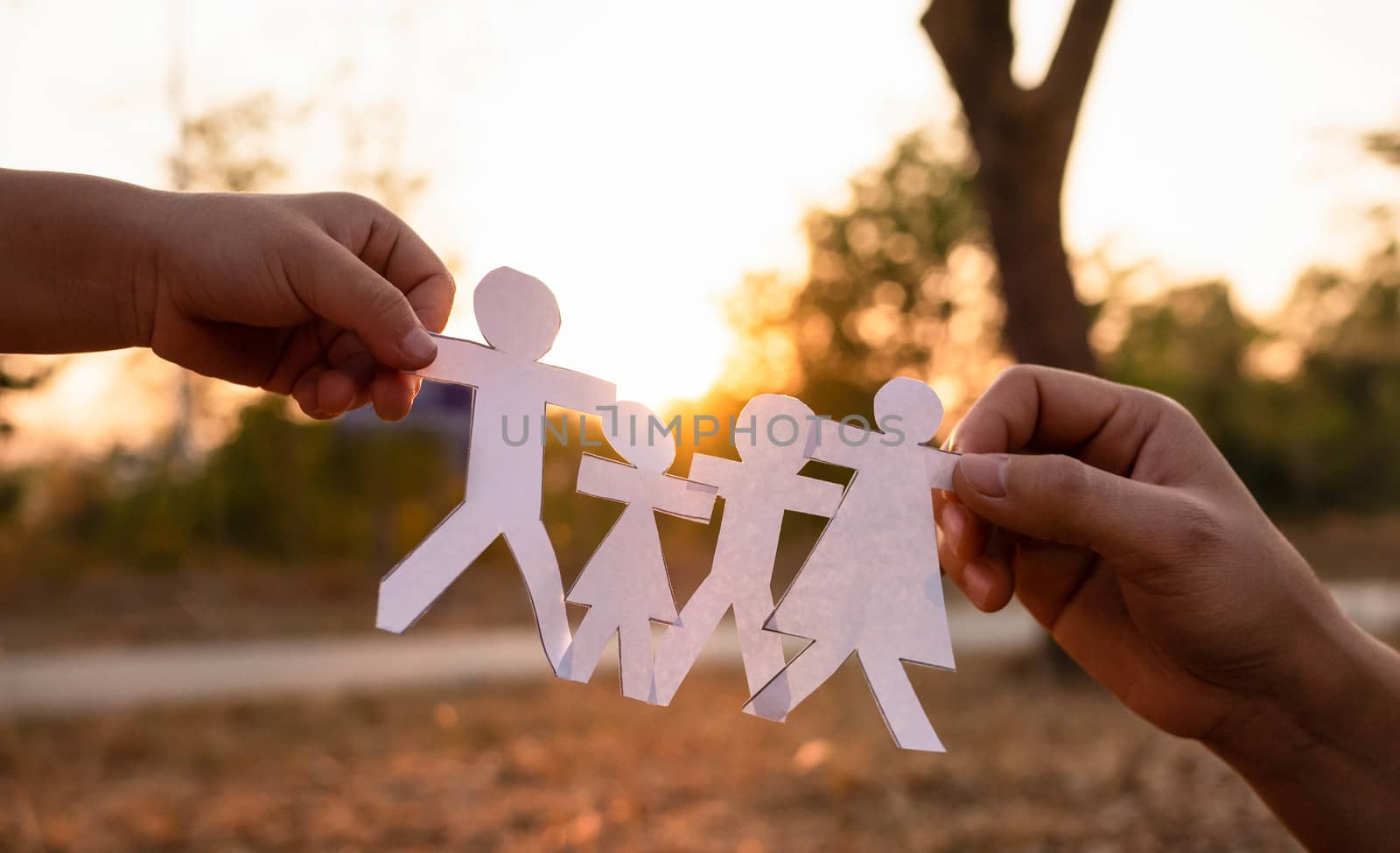 Hands of mother and daughter holding family cut out paper in autumn park on sunset background. by TEERASAK
