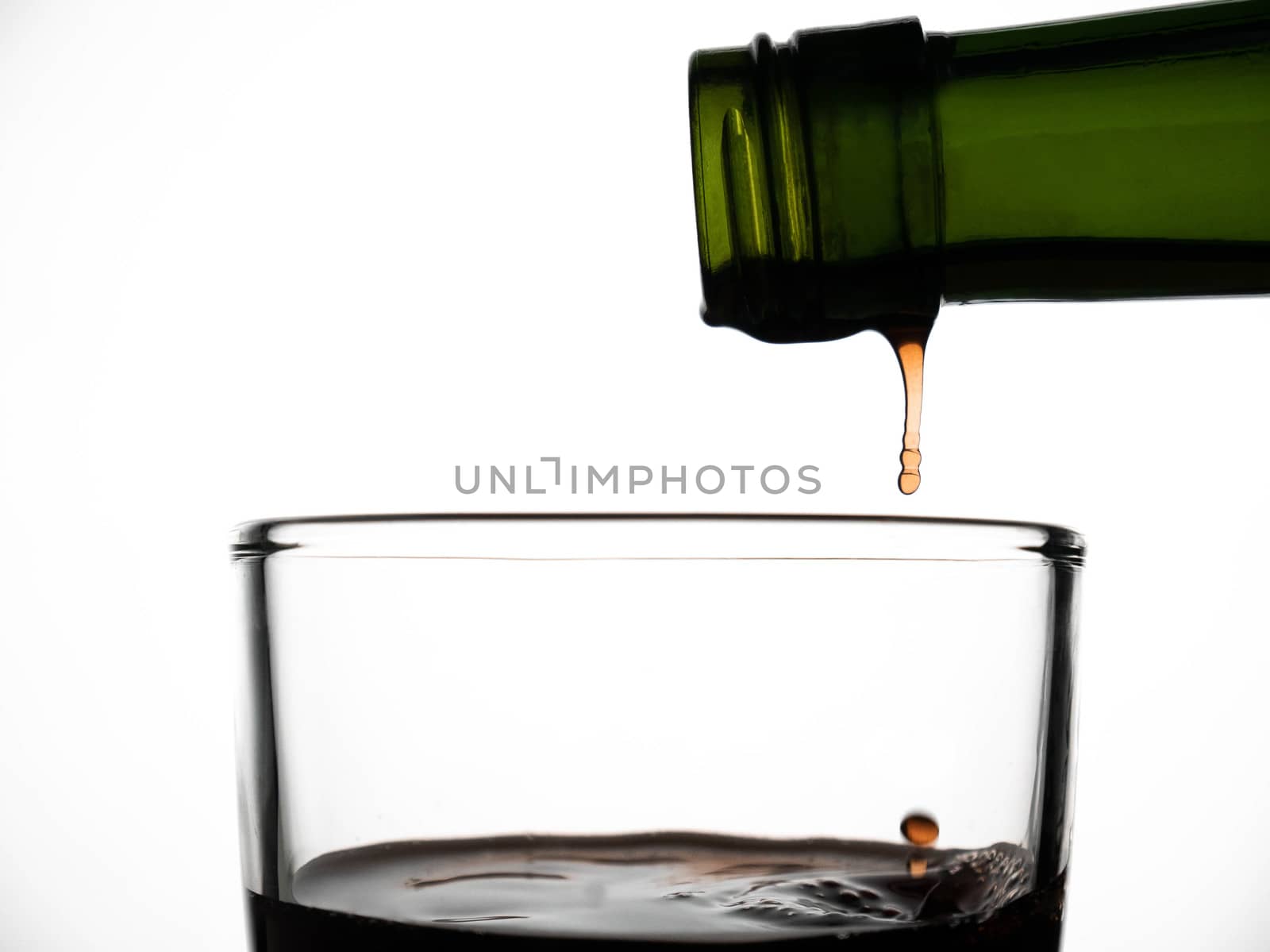 Close up of pouring fruit juice from green bottle into glass, isolated on white background. by TEERASAK