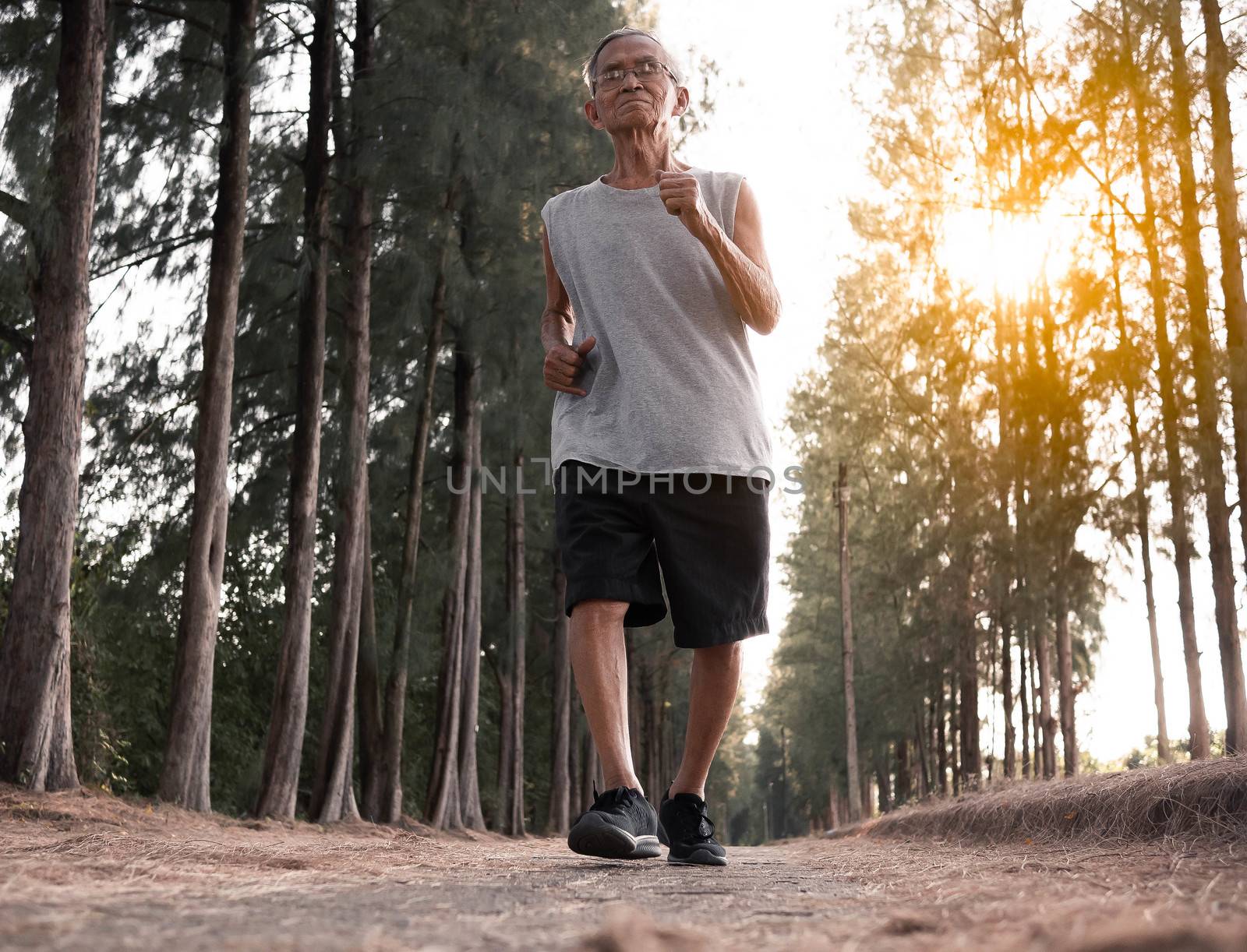 Asian senior man jogging in the park over sunset sky background. Healthy lifestyle and Healthcare concept. by TEERASAK