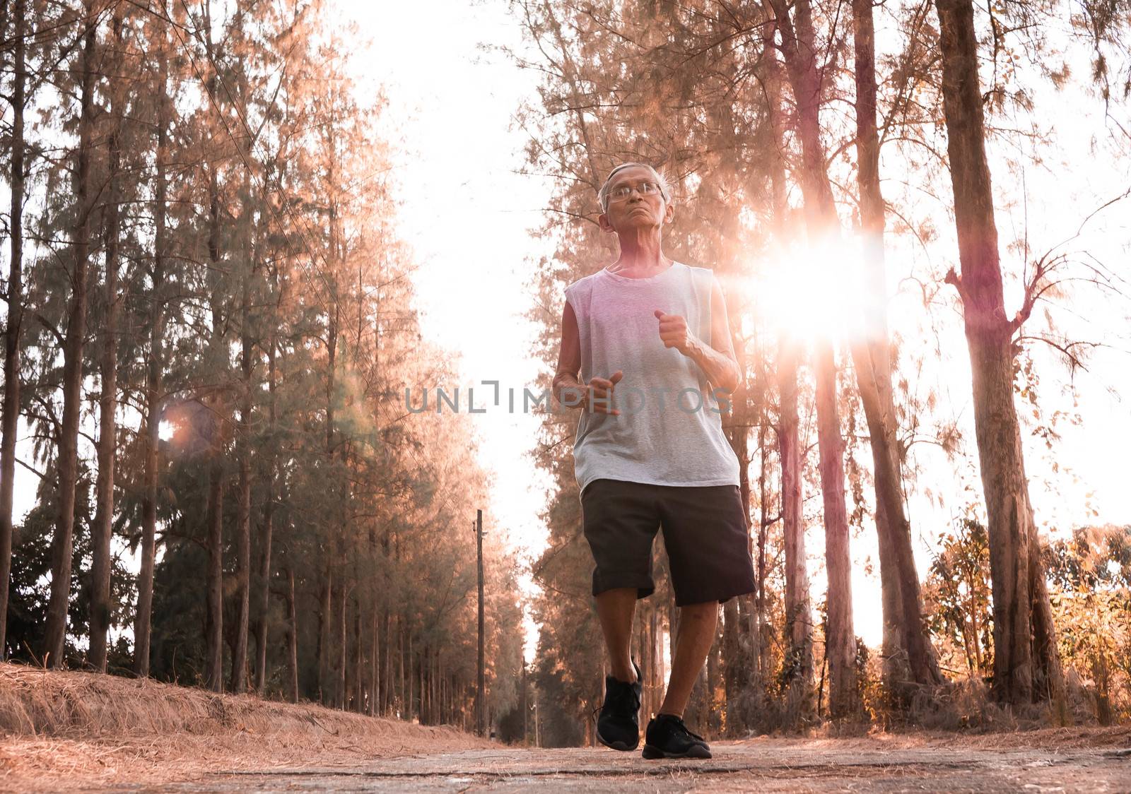 Asian senior man jogging in the park over sunset sky background. by TEERASAK