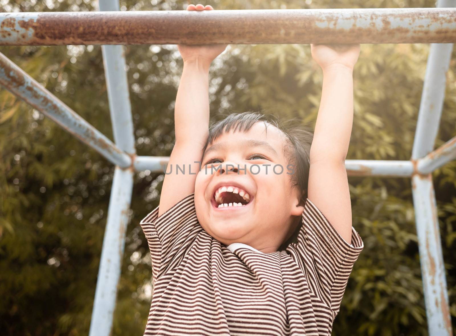 Cute Asian little girl hanging the monkey bars by her hand to exercise at out door playground on sunny day. by TEERASAK