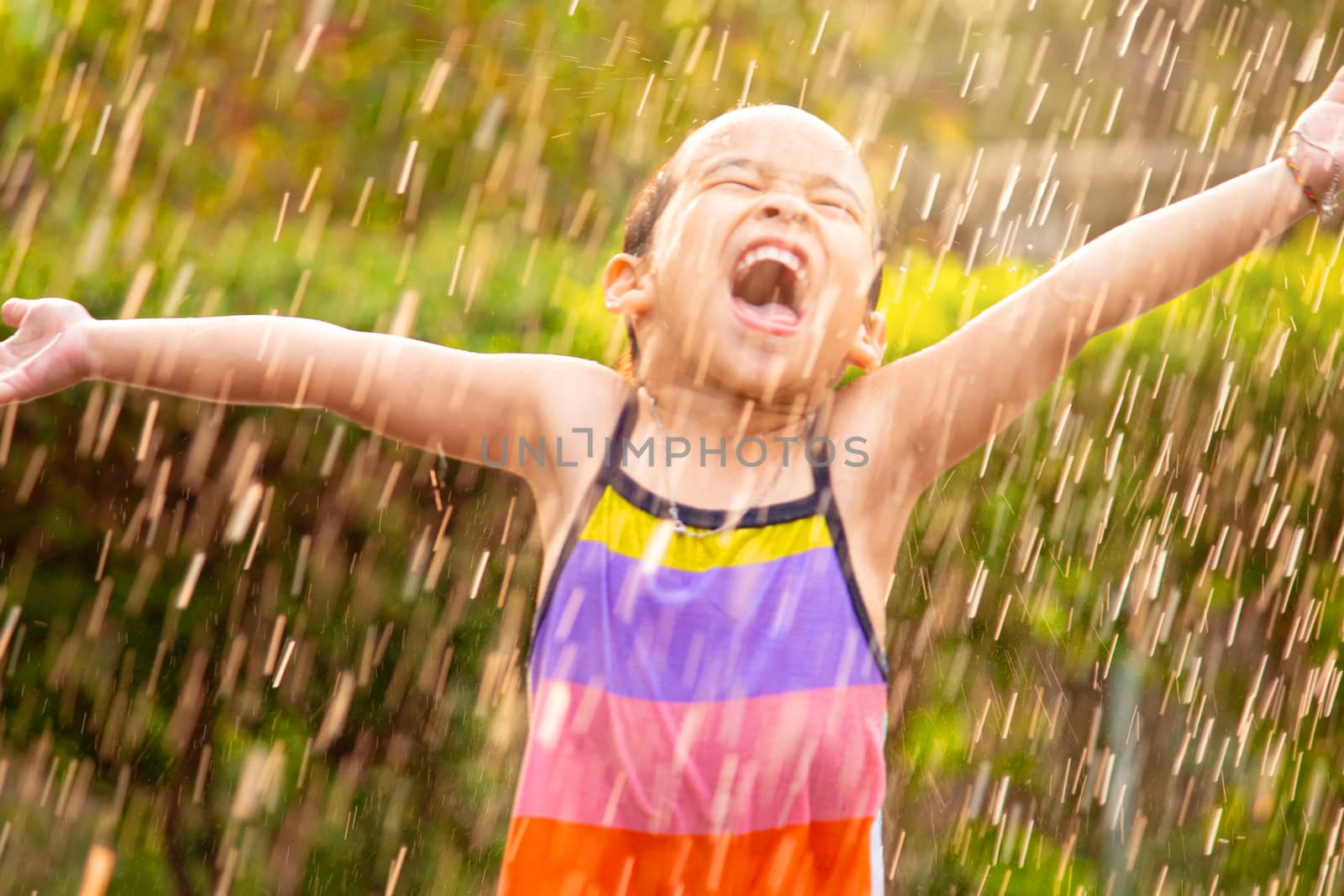 Cute little girl having fun in rainy at backyard. Children enjoy outdoor activities on hot summer days.