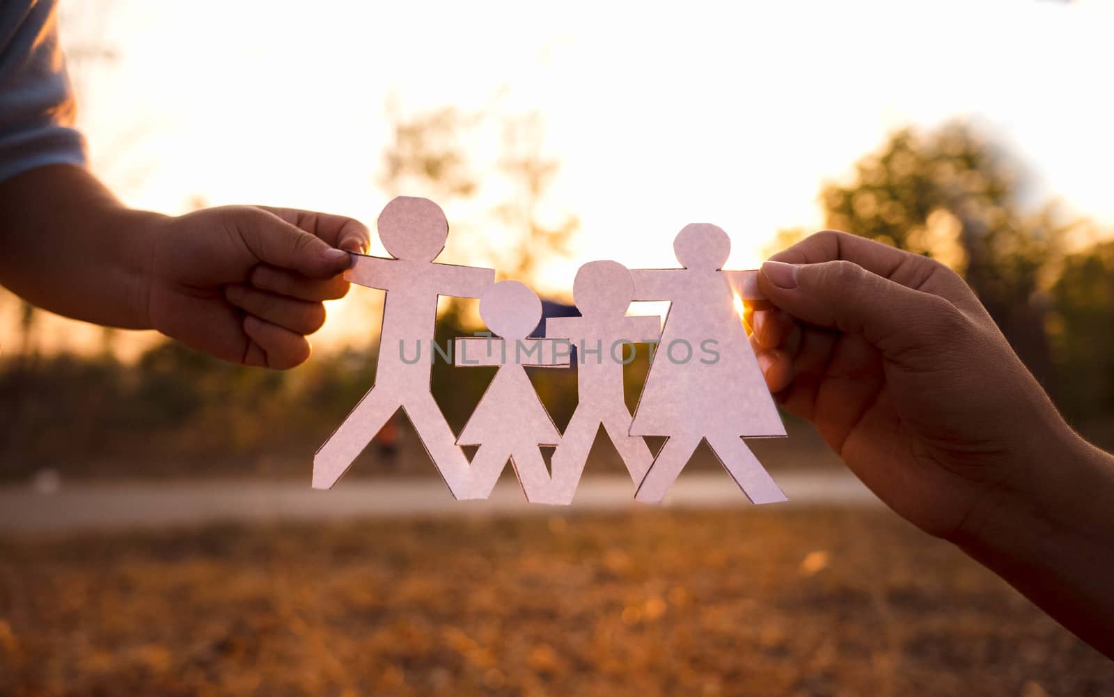 Hands of mother and daughter holding family cut out paper in autHands of mother and daughter holding family cut out paper in autumn park on sunset background. by TEERASAK