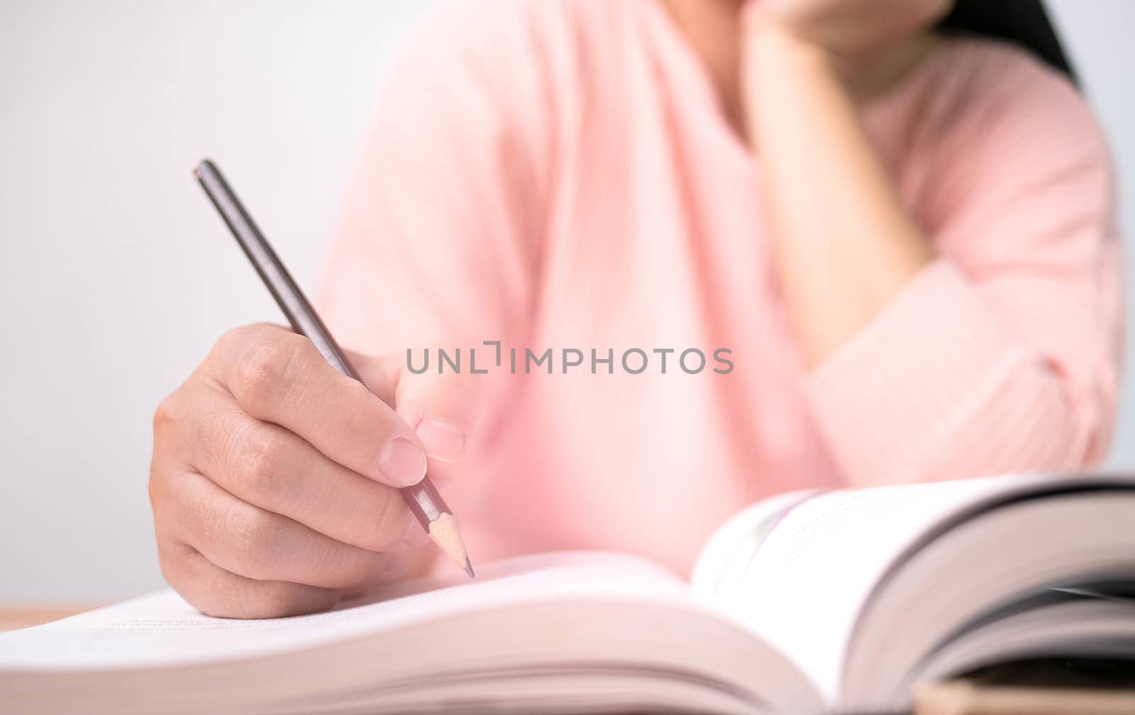 Close up of Woman's hand drawing a line and writing short summary while reading a book at library.