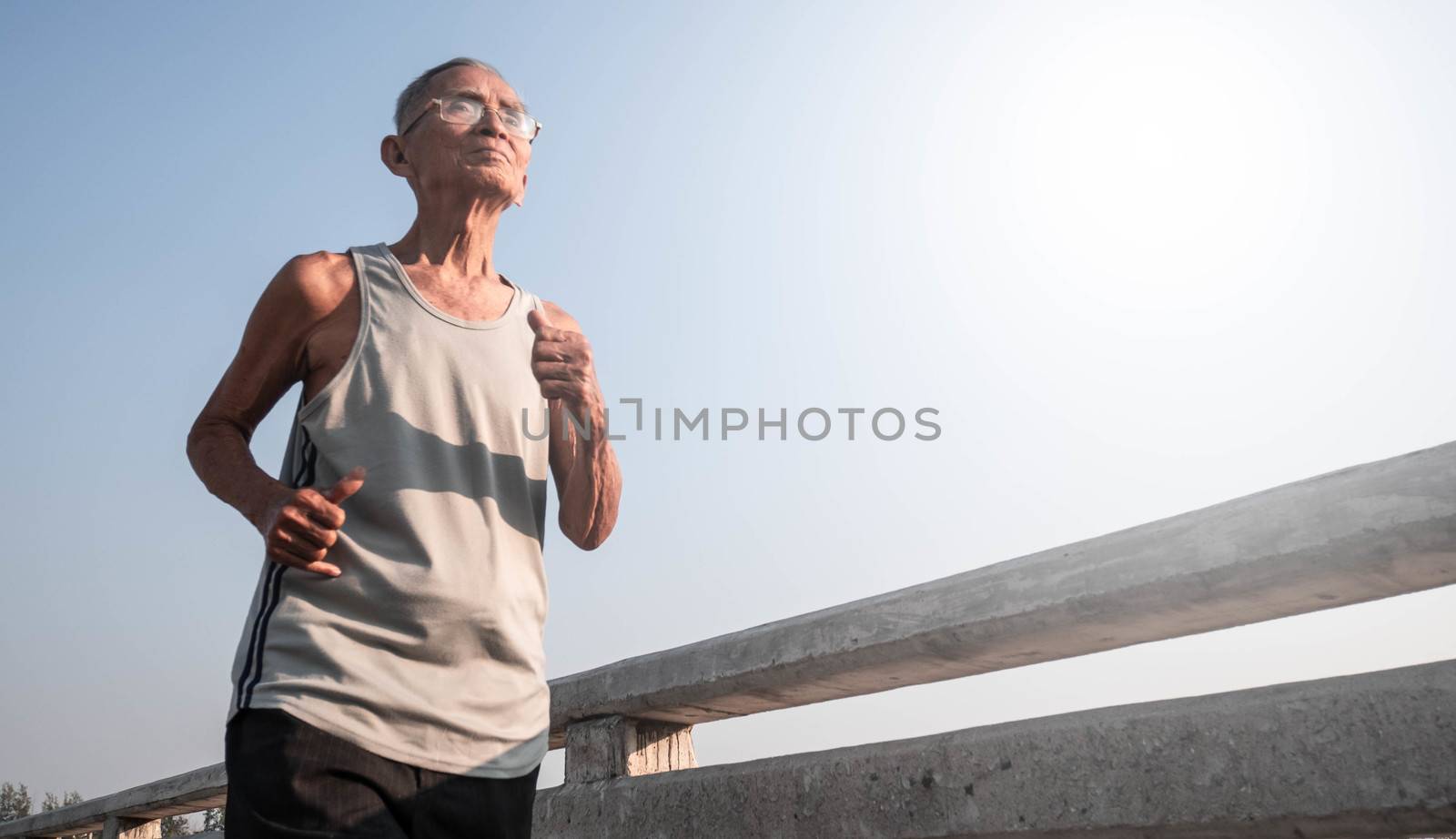 Asian senior man in sportswear jogging on bridge over sky background. Healthy lifestyle and Healthcare concept. by TEERASAK