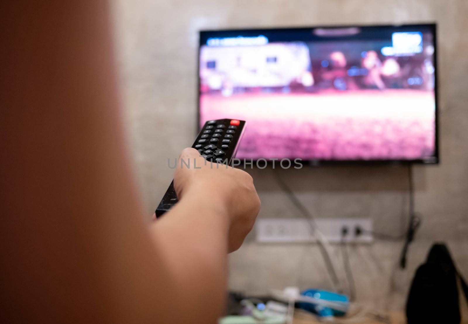 Asian young woman watching TV in the room with remote control in her hand to adjust volume or changing TV channel. Relaxation in living room. Selective focus.