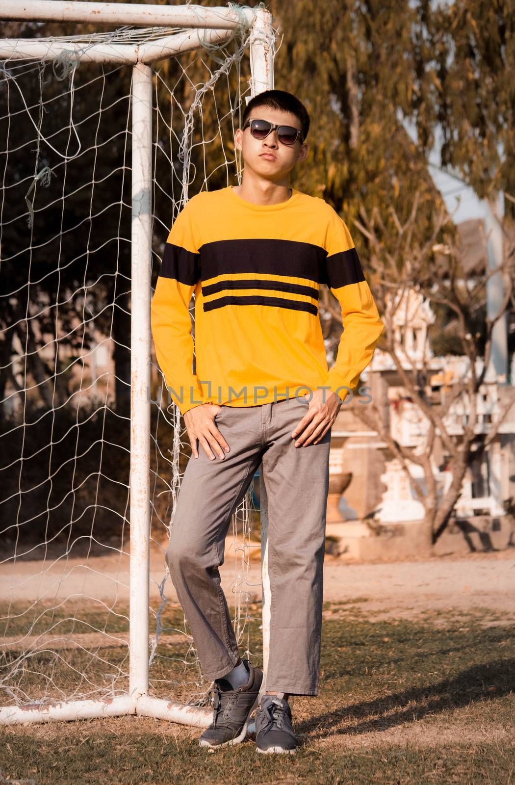 Portrait of a young handsome teenager boy in yellow long sleeve t-shirt and wear black glasses, stand in the park. lifestyle people concept.