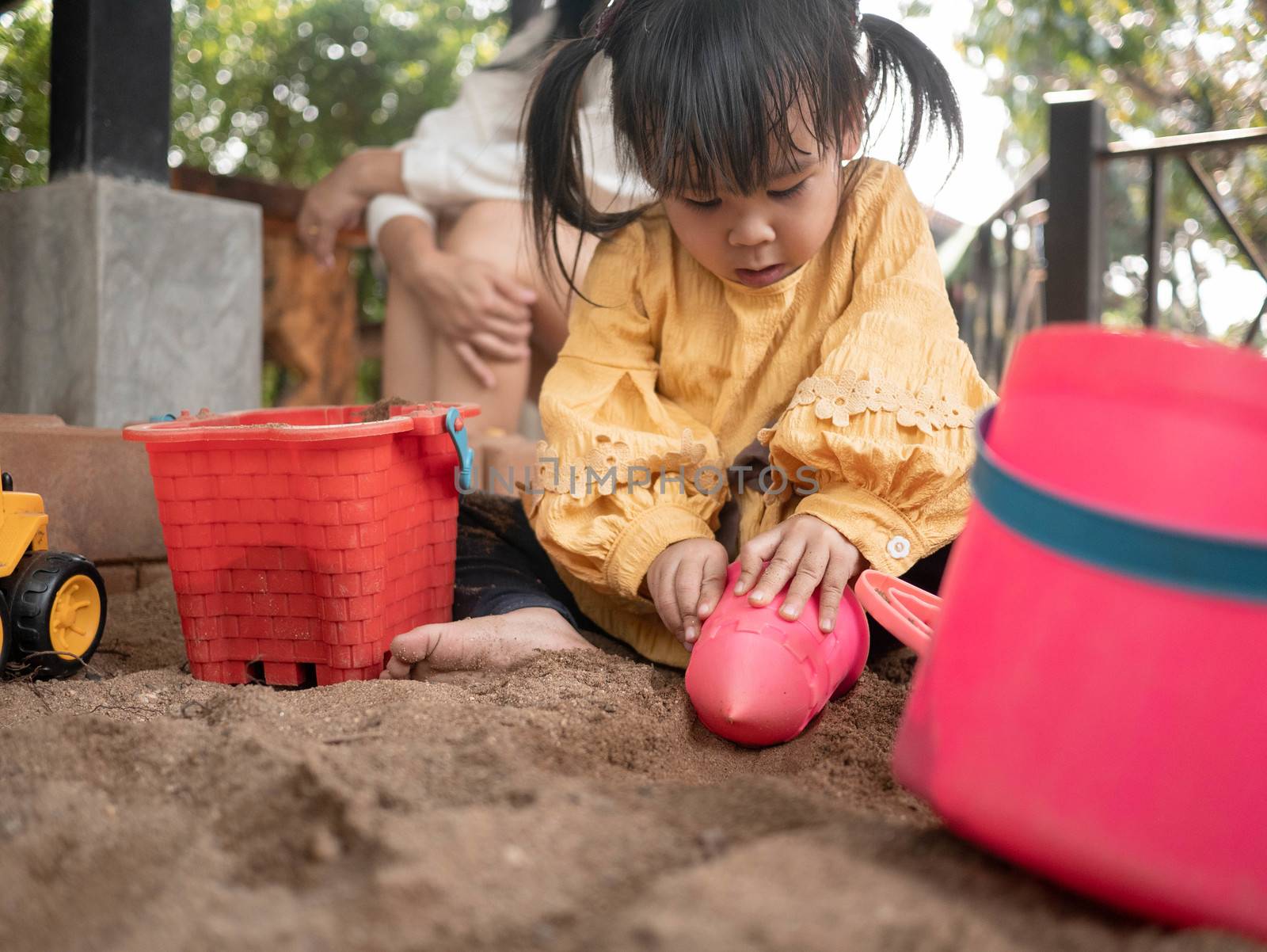 Happy little child girl having fun playing with plastic toys sitting in the sandbox on a sunny summer day. by TEERASAK