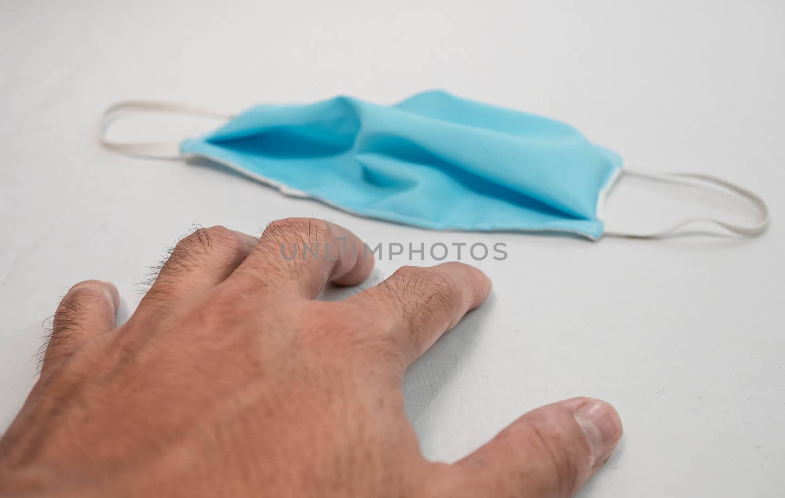 Human reaching out your hand to pick a homemade cloth face mask that placed on table, use for protection from air pollution or virus epidemic. Scarce medical mask concept. by TEERASAK