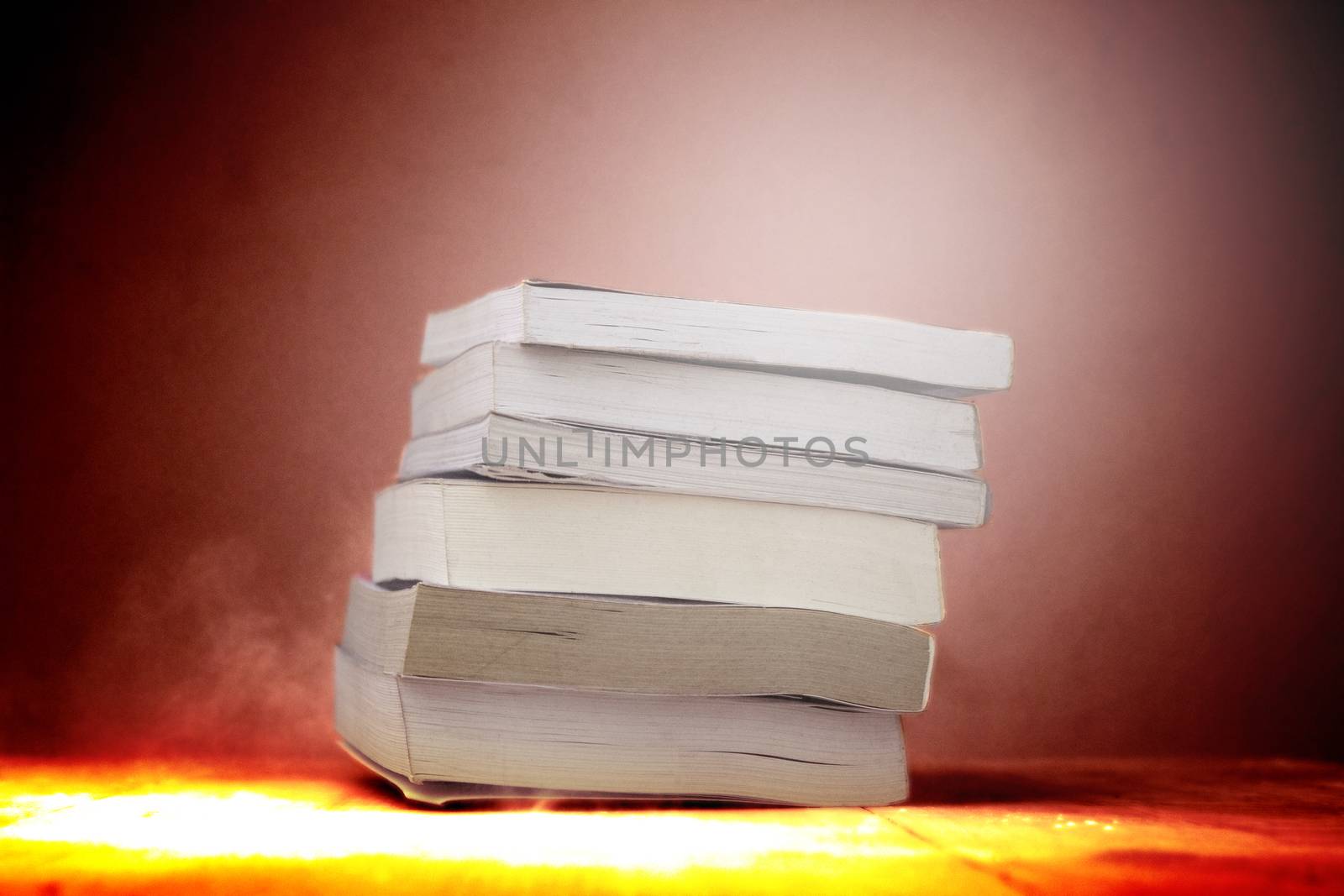 A stack of books resting on a dusty desk in room. by TEERASAK