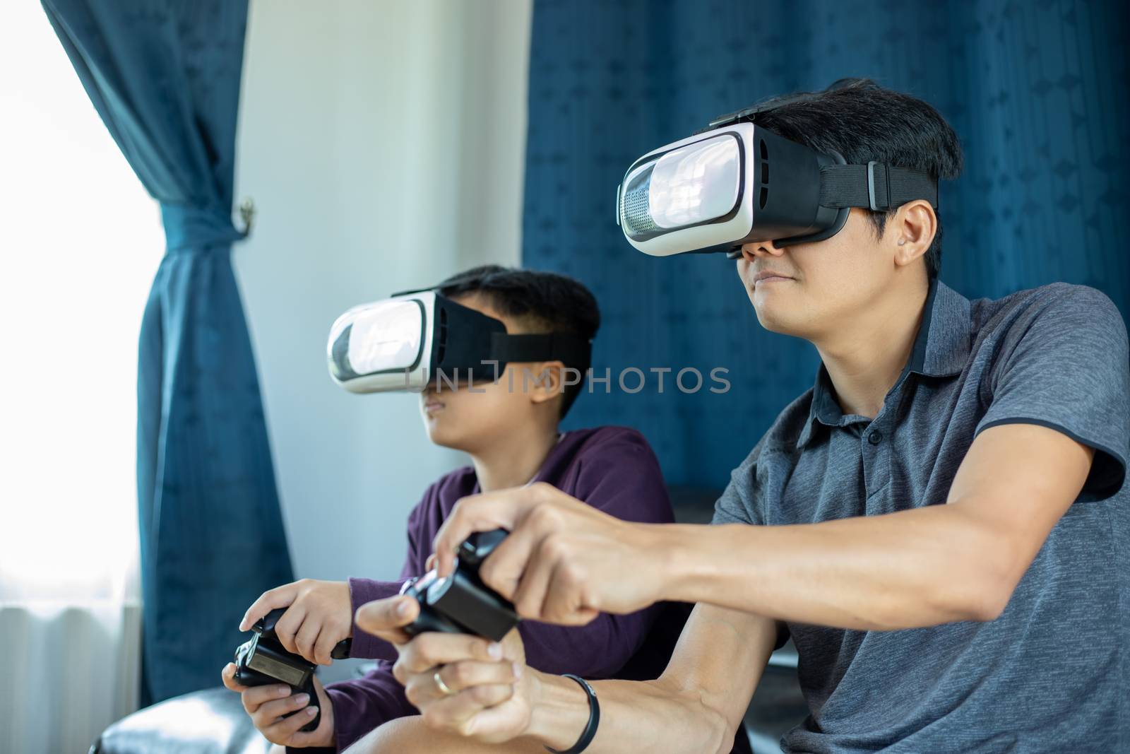 Asian father and son enjoy playing video games together with video joystick and Virtual Reality Glasses with exciting and very fun in the living room at home