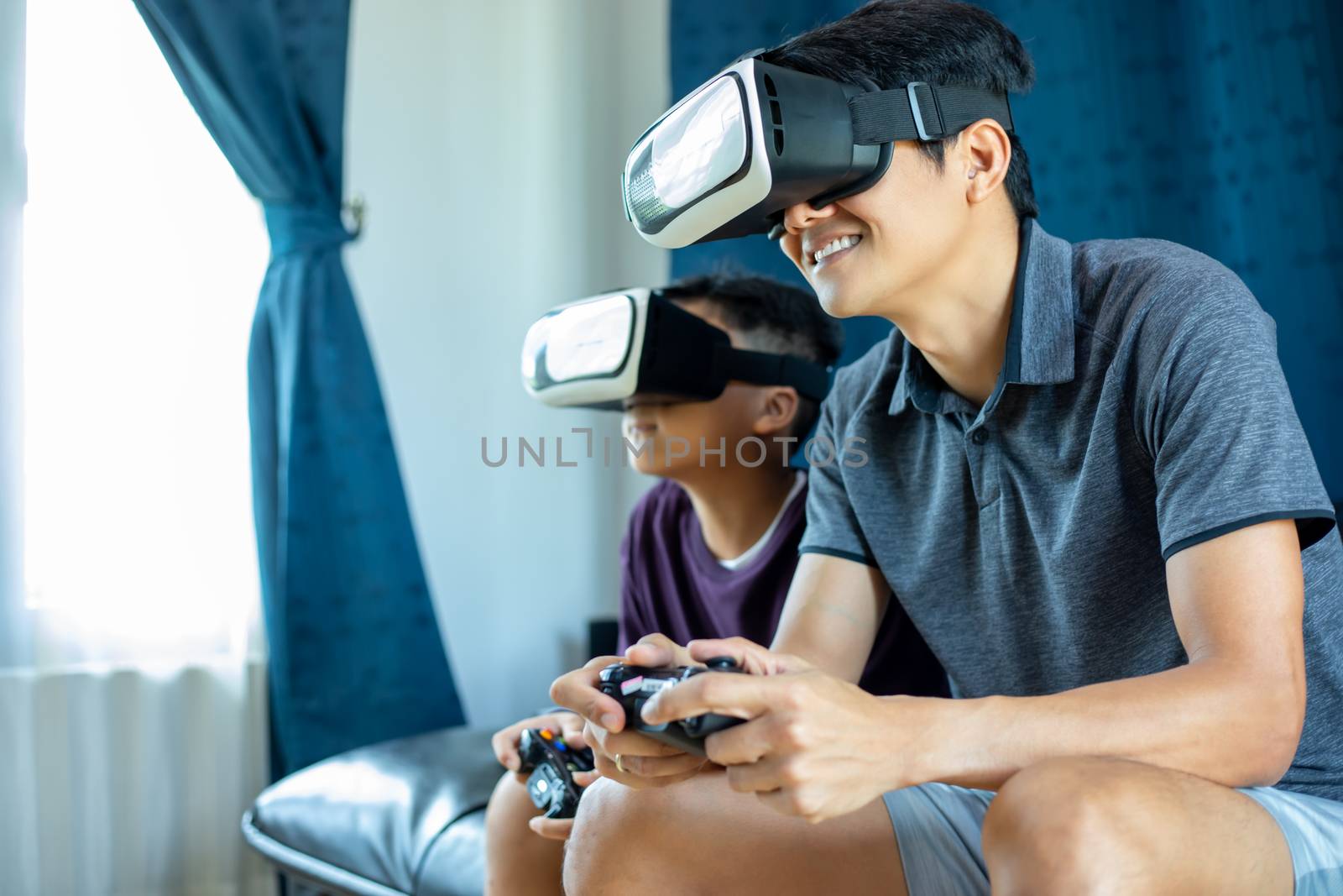 Asian father and son enjoy playing video games together with video joystick and Virtual Reality Glasses with exciting and very fun in the living room at home